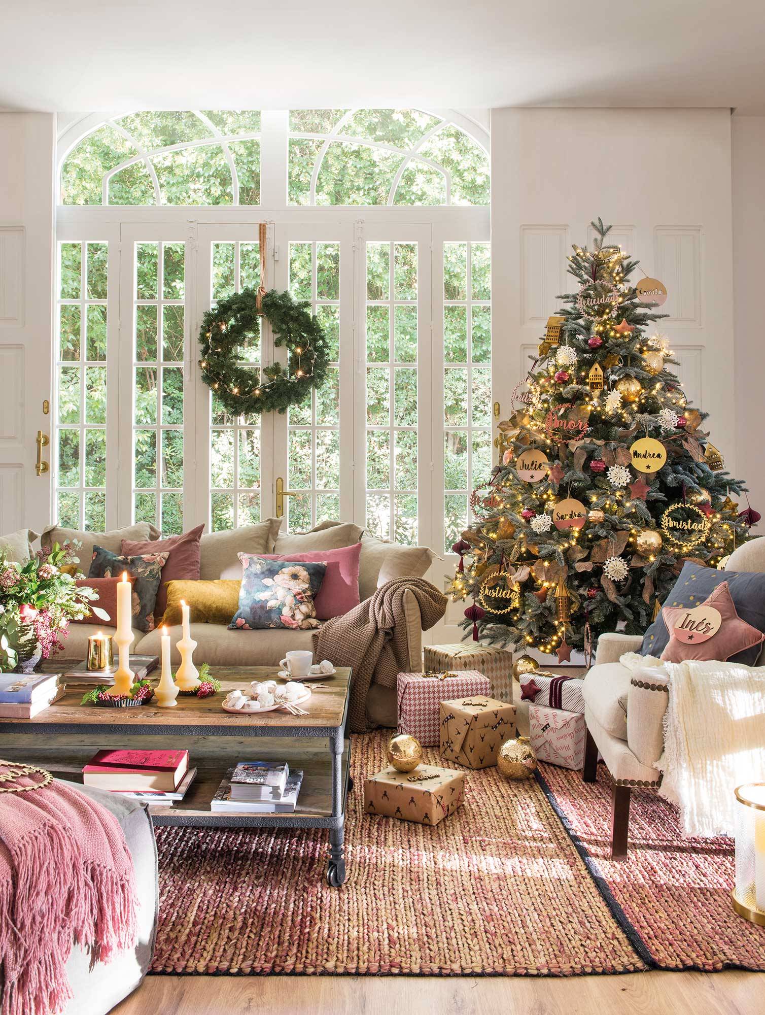 Salón colorido con ventanal, mesa de madera, alfombra de fibras y árbol de Navidad con adornos personales en rosa y dorado. 