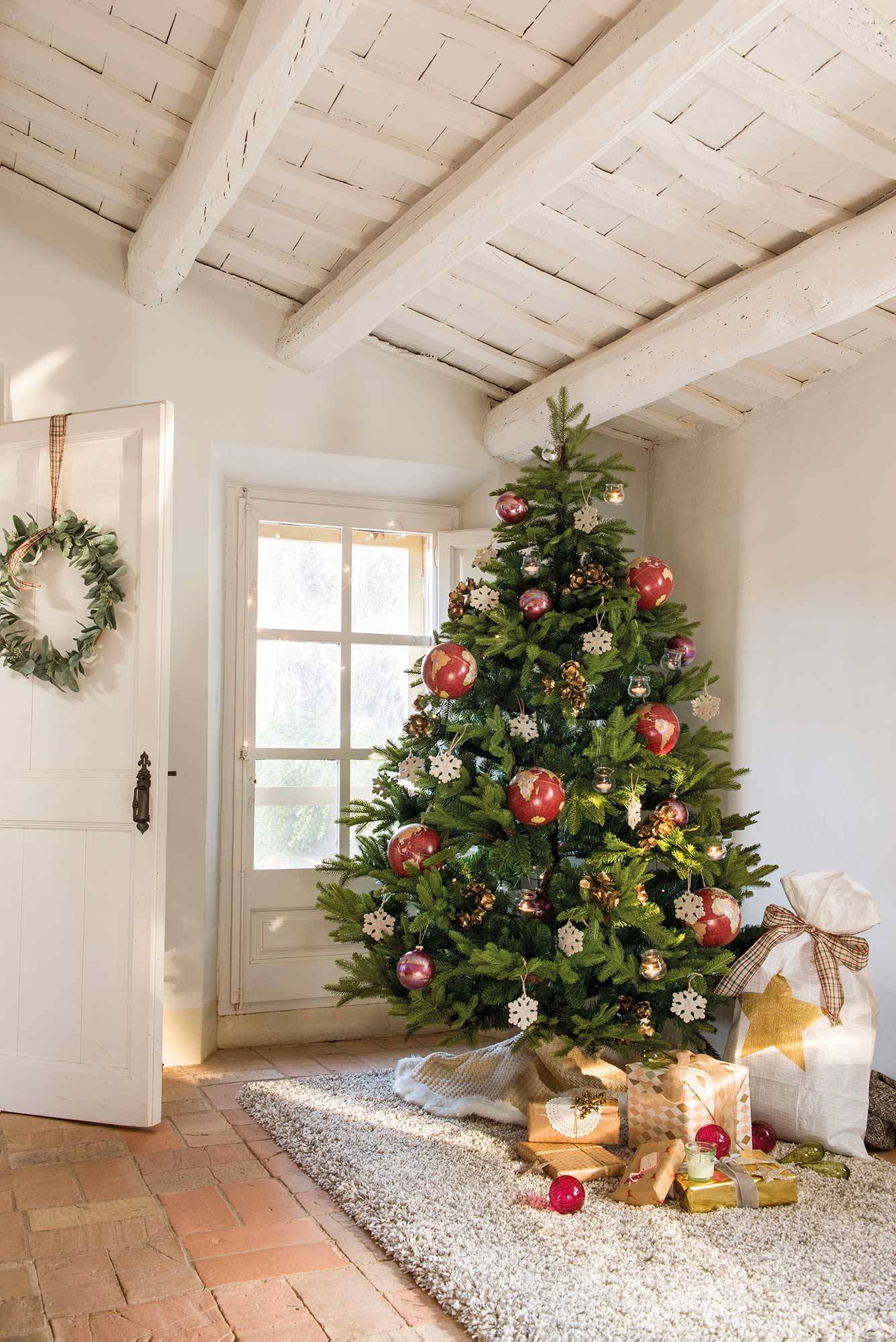 Recibidor con árbol de Navidad decorado con adornos, alfombra y techo con vigas de madera en blanco. 