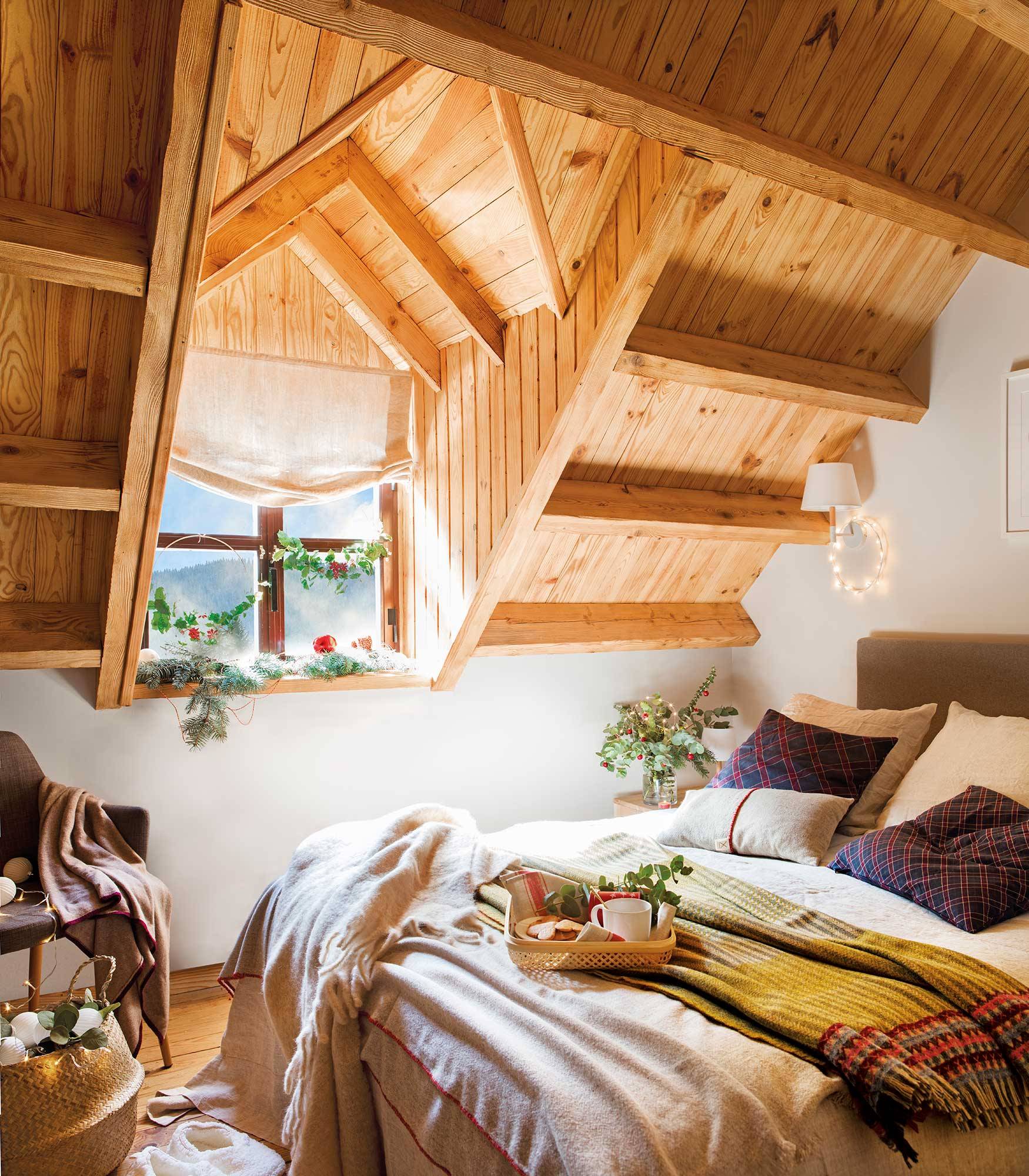 Dormitorio abuhardillado con techo de madera decorado por Navidad.