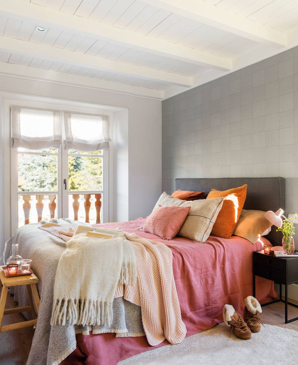 dormitorio-con-techo-de-vigas-blanco-cabecero-y-banco-de-madera-y-estores-en-la-ventana.