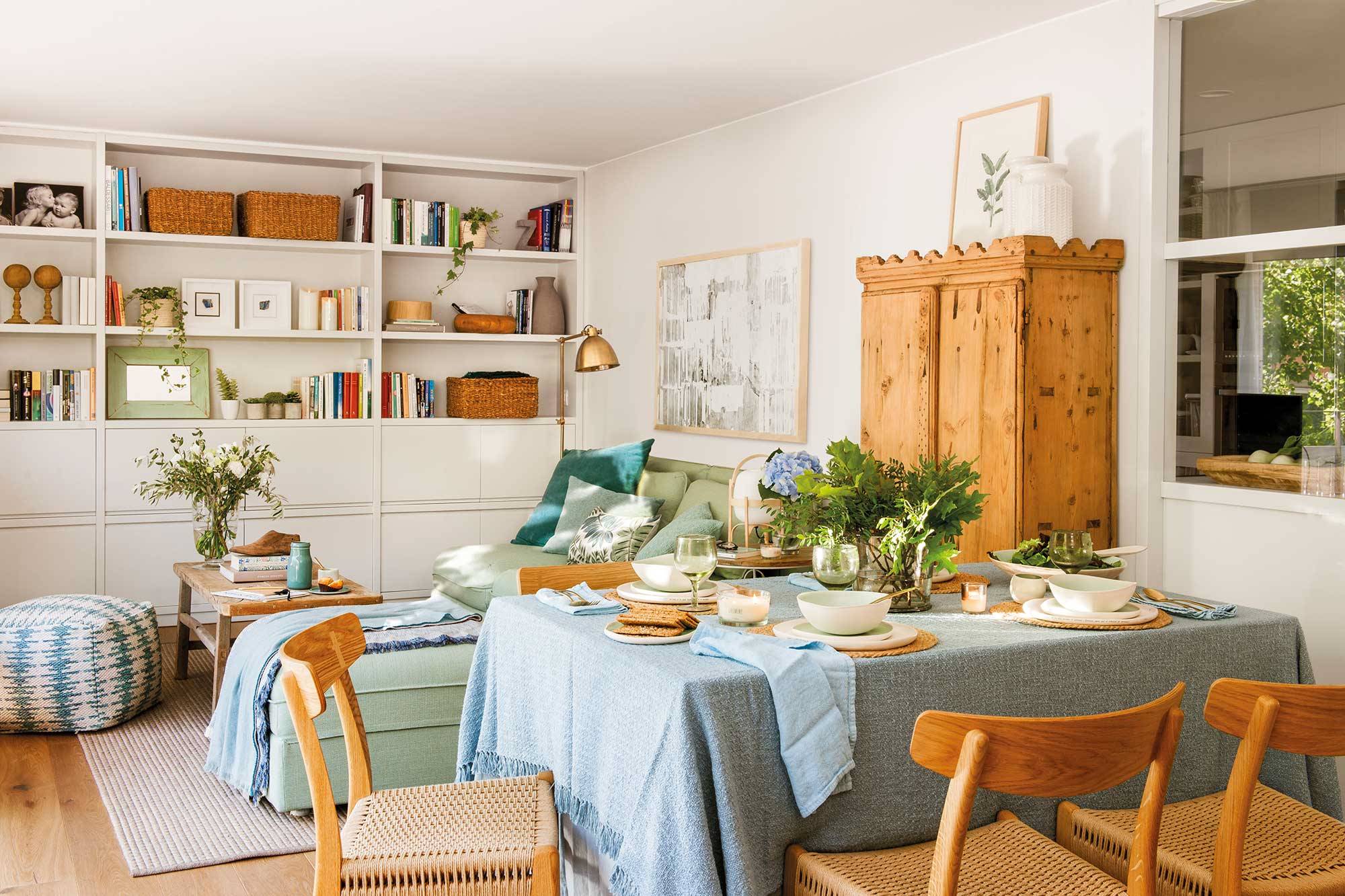 Salón comedor pequeño con estantería de pared a pared y sofá verde modular.