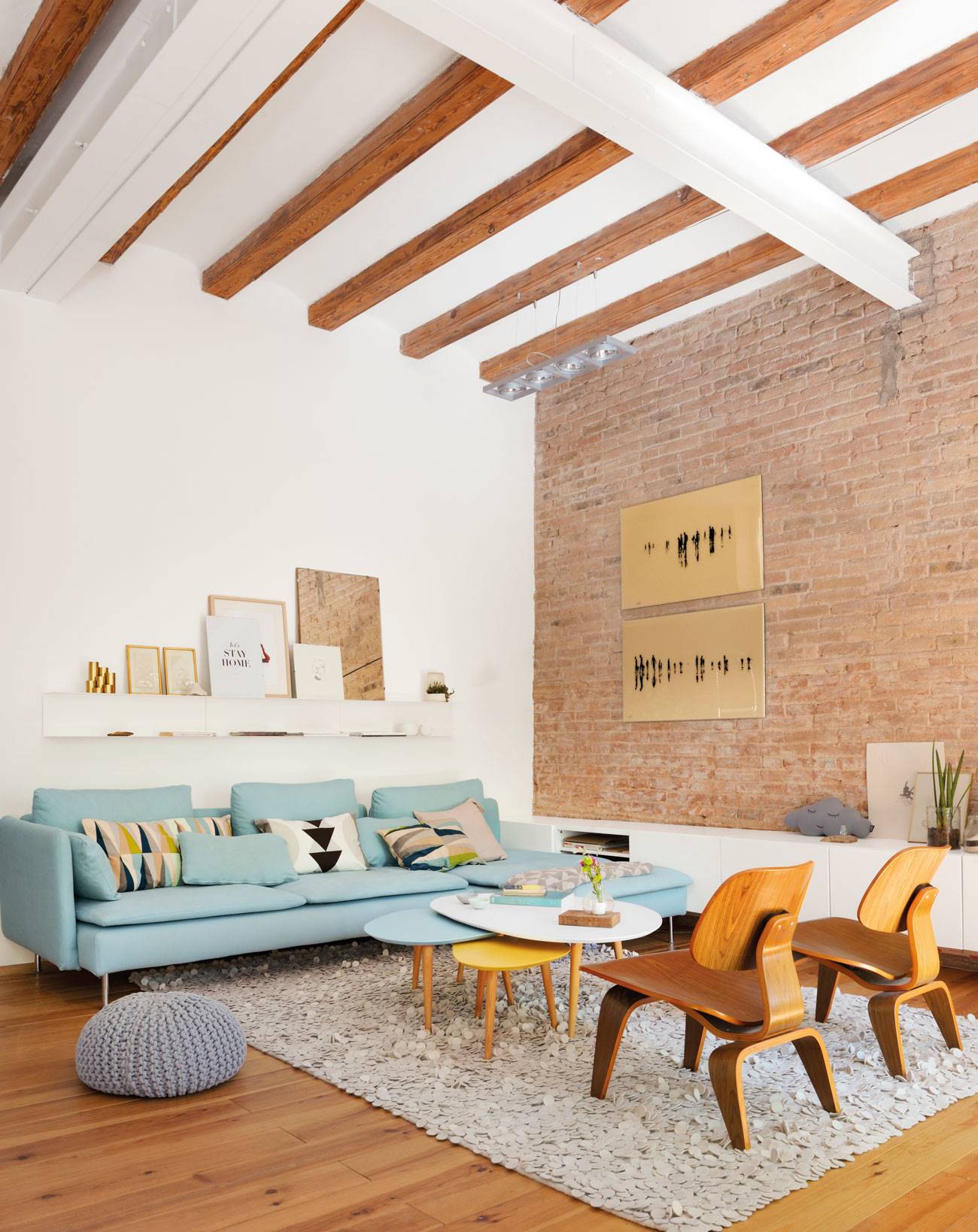 Salón moderno con pared de ladrillo, alfombra, suelo de madera y vigas. Sofá azul claro con chaise longue.