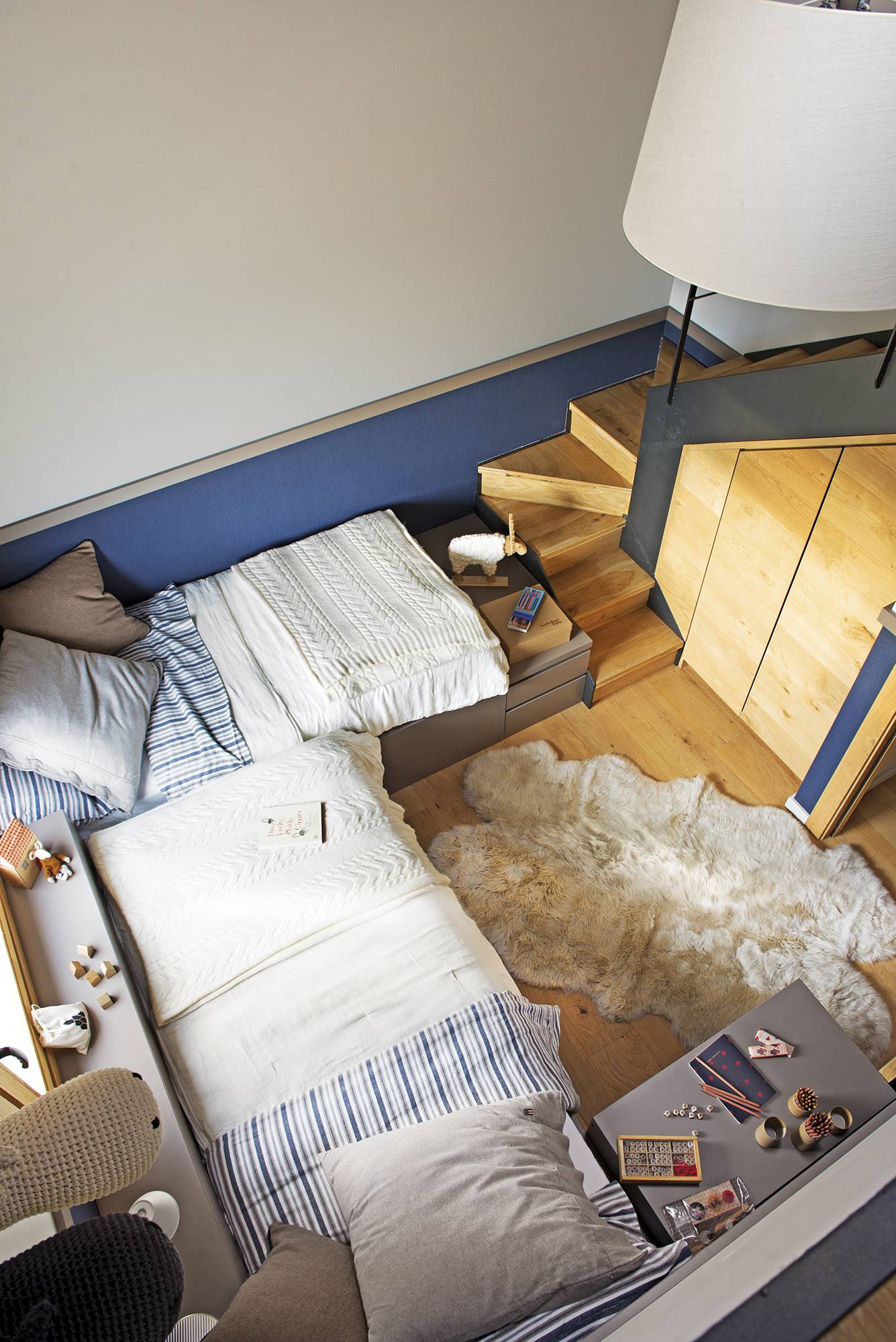Vista cenital de dormitorio infantil con dos camas en "L" y arrimadero azul. 