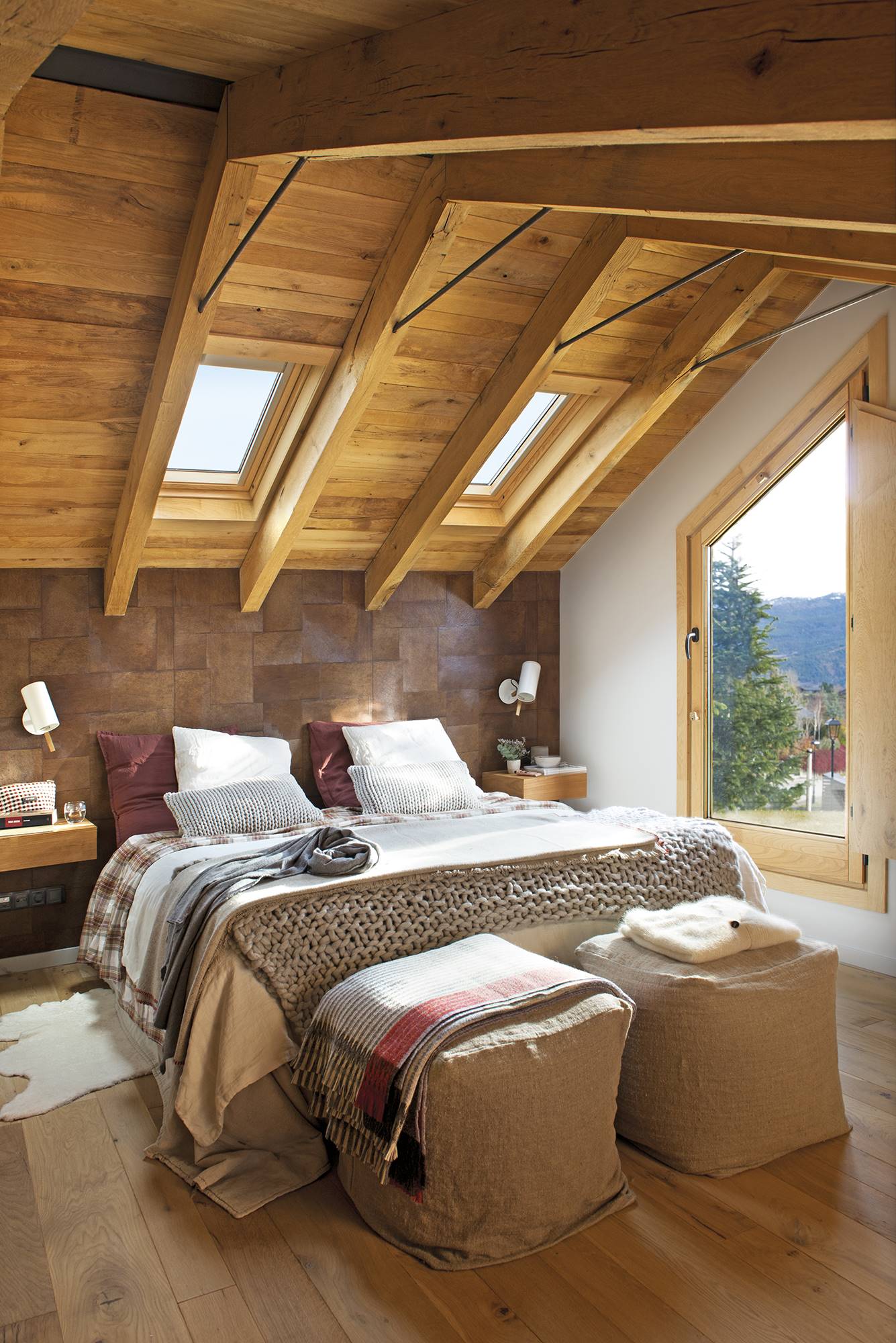 Dormitorio abuhardillado de casa de montaña con vigas de madera y papel pintado en el cabecero. 
