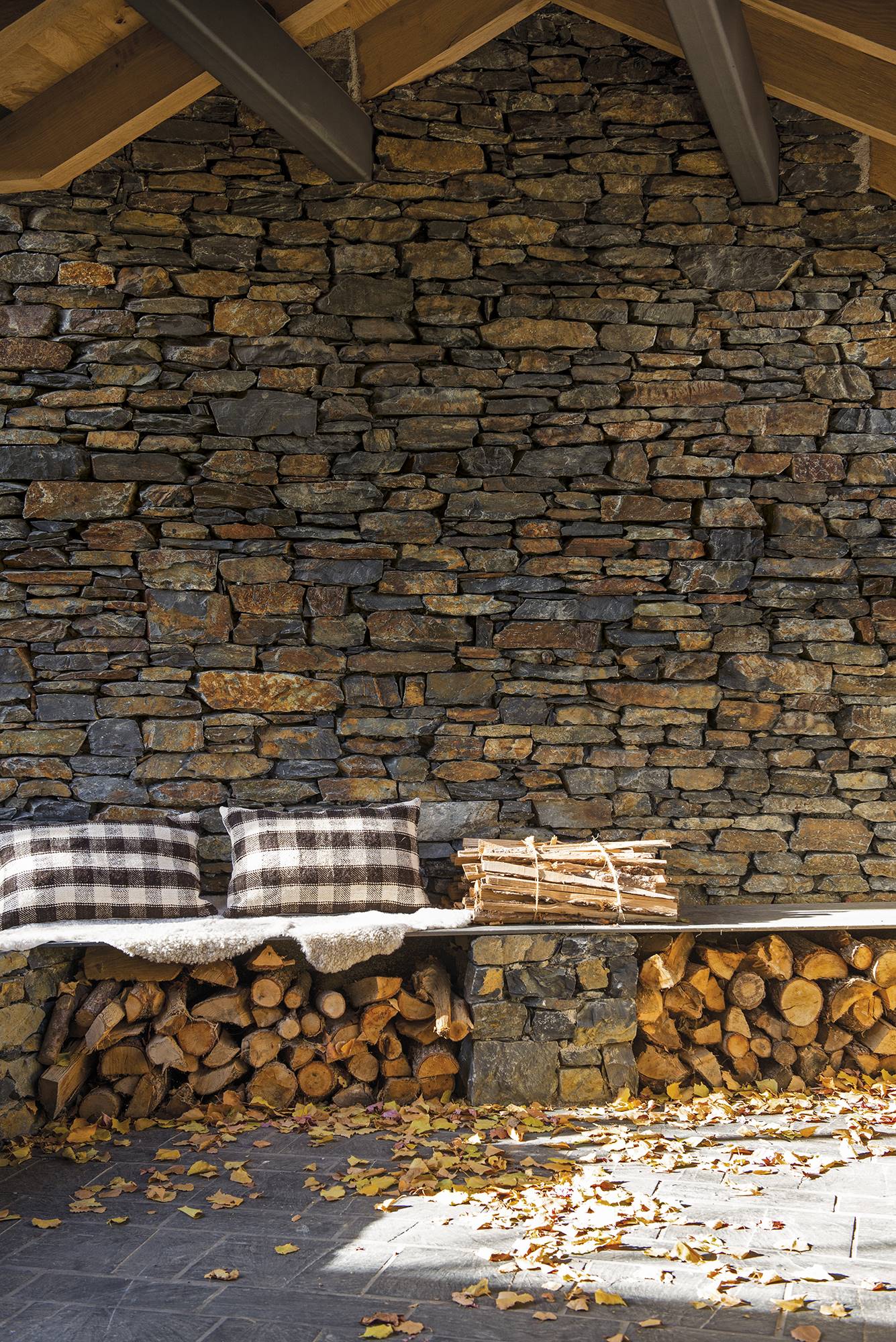 Exterior de casa de montaña de piedra con leñero de hierro con sobre a modo de banco.