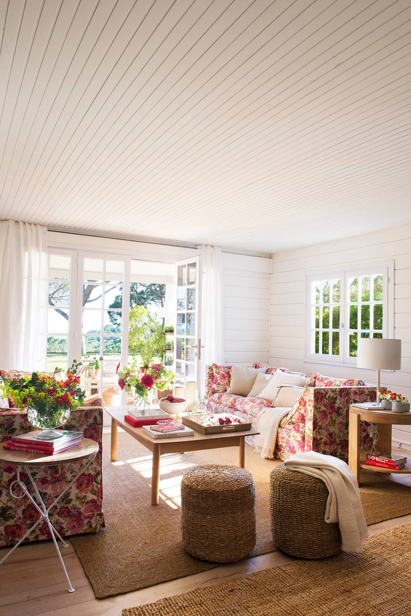 Salón de casa con paredes de madera blanca y sofás a flores.