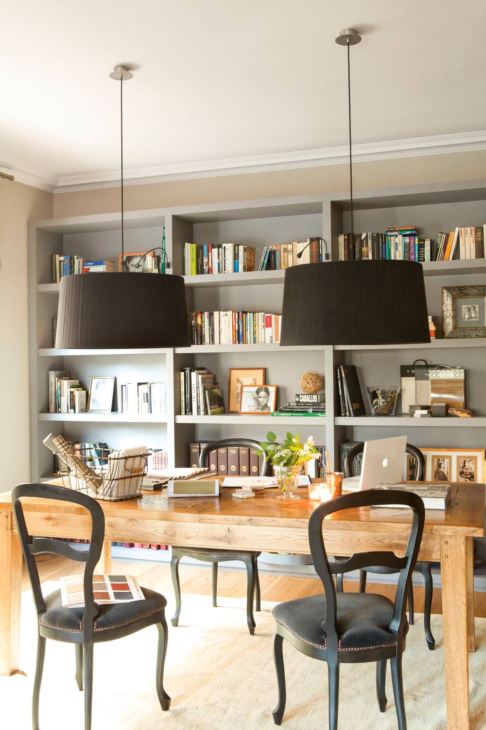 Comedor con librería en gris, sillas en gris y lámparas negras.