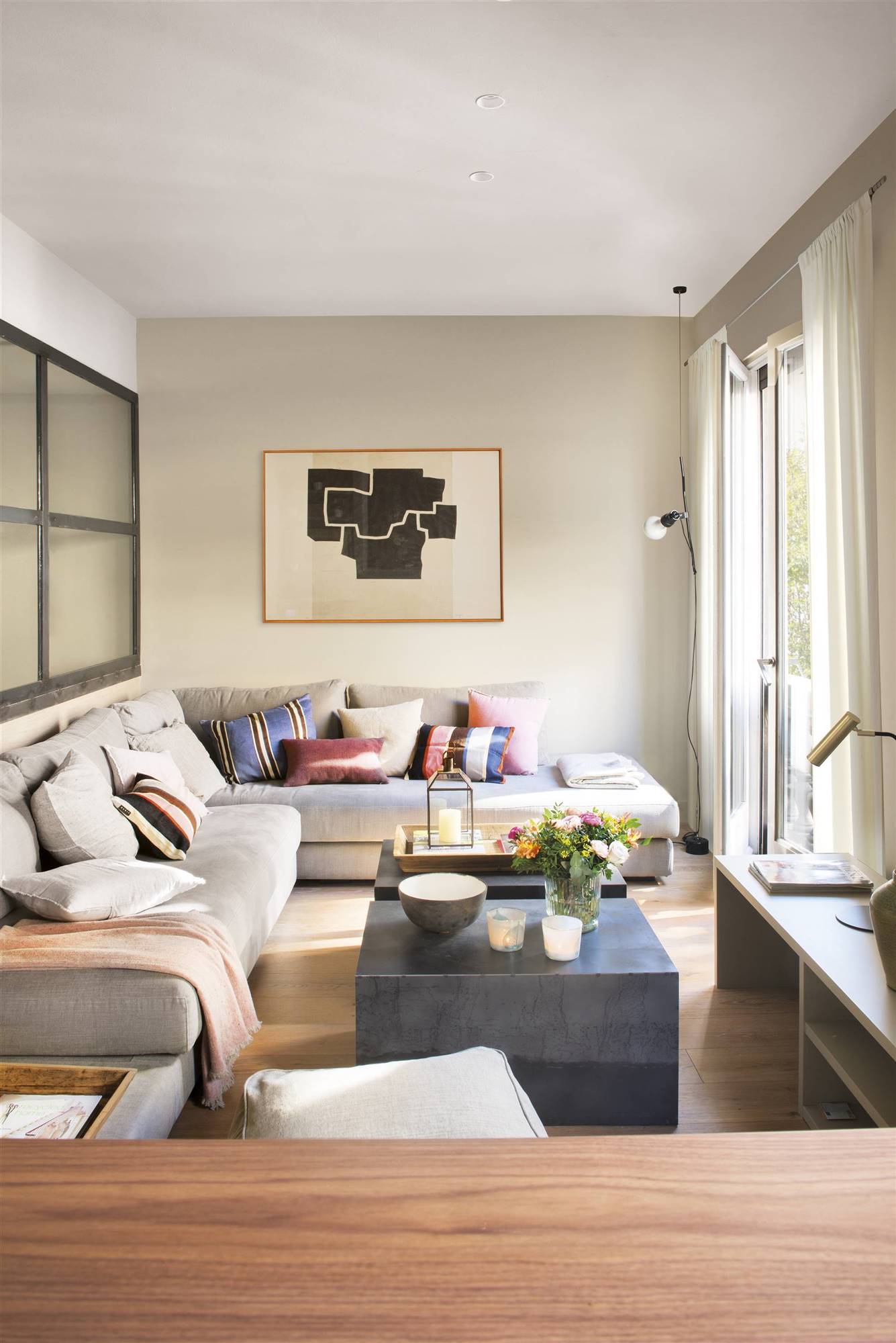 Salón pequeño con un sofá chaiselongue gris, mesa de centro diseñada a medida en negro y cuadro en la pared. 