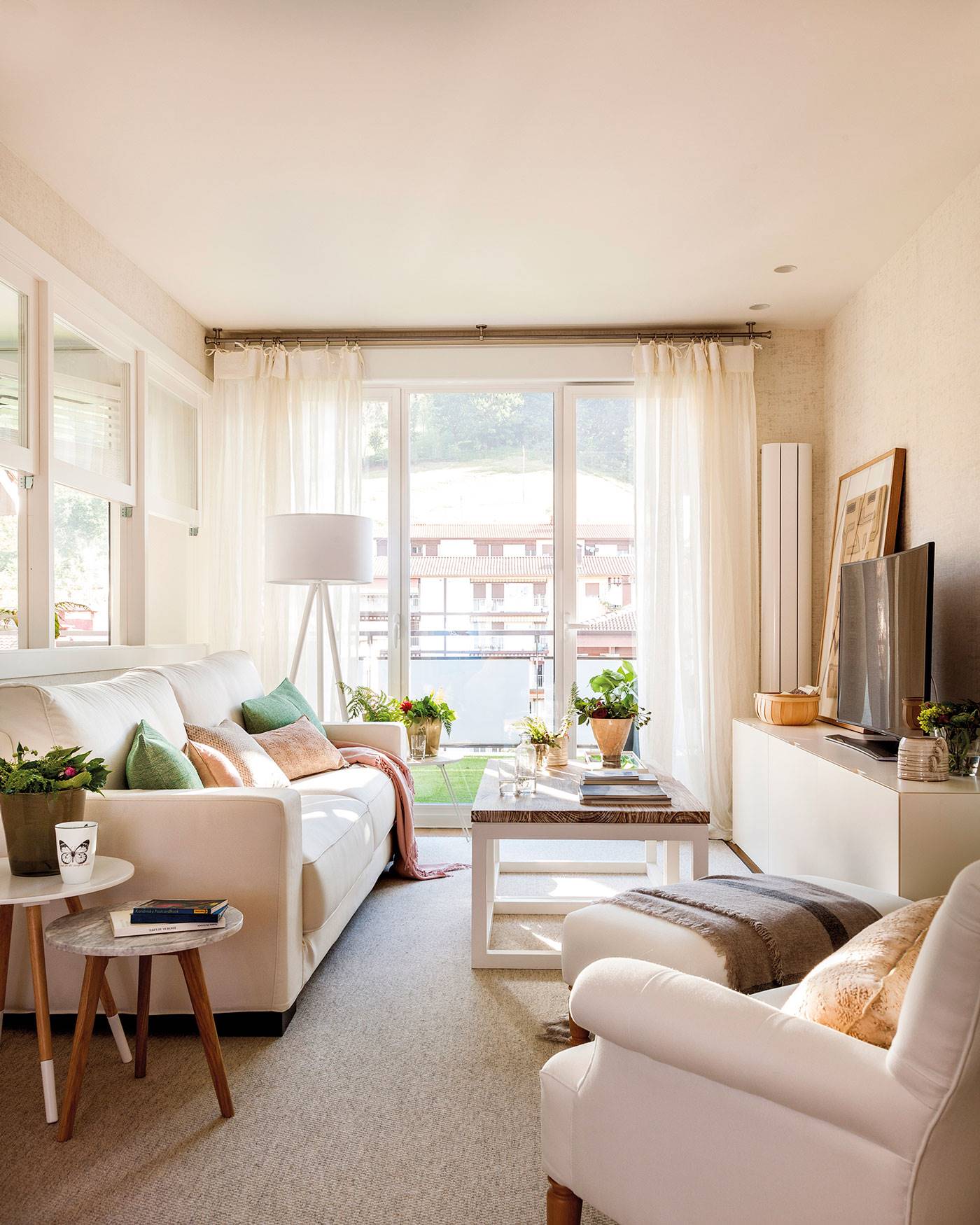 Salón pequeño con gran ventana y sofás blancos. 