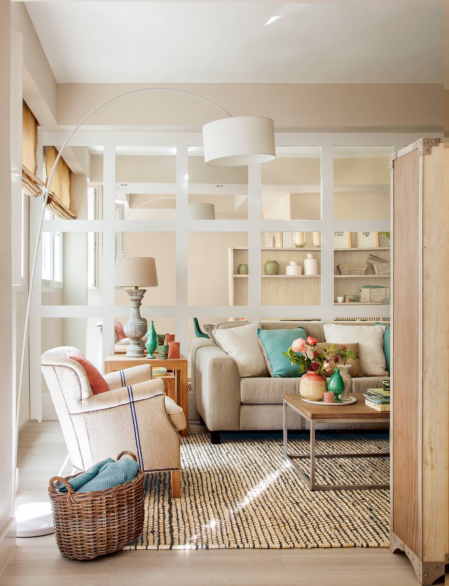 Salón pequeño con pared forrada de espejo y sofá y butacas de color beige. 