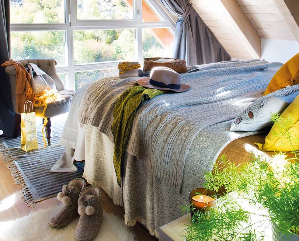 Dormitorio abuhardillado de casa de montaña con gran ventanal a pie de cama