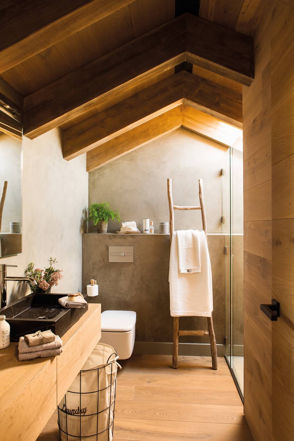 Baño reformado con revestimiento de madera, ducha con mampara de cristal y lavamanos negro. 
