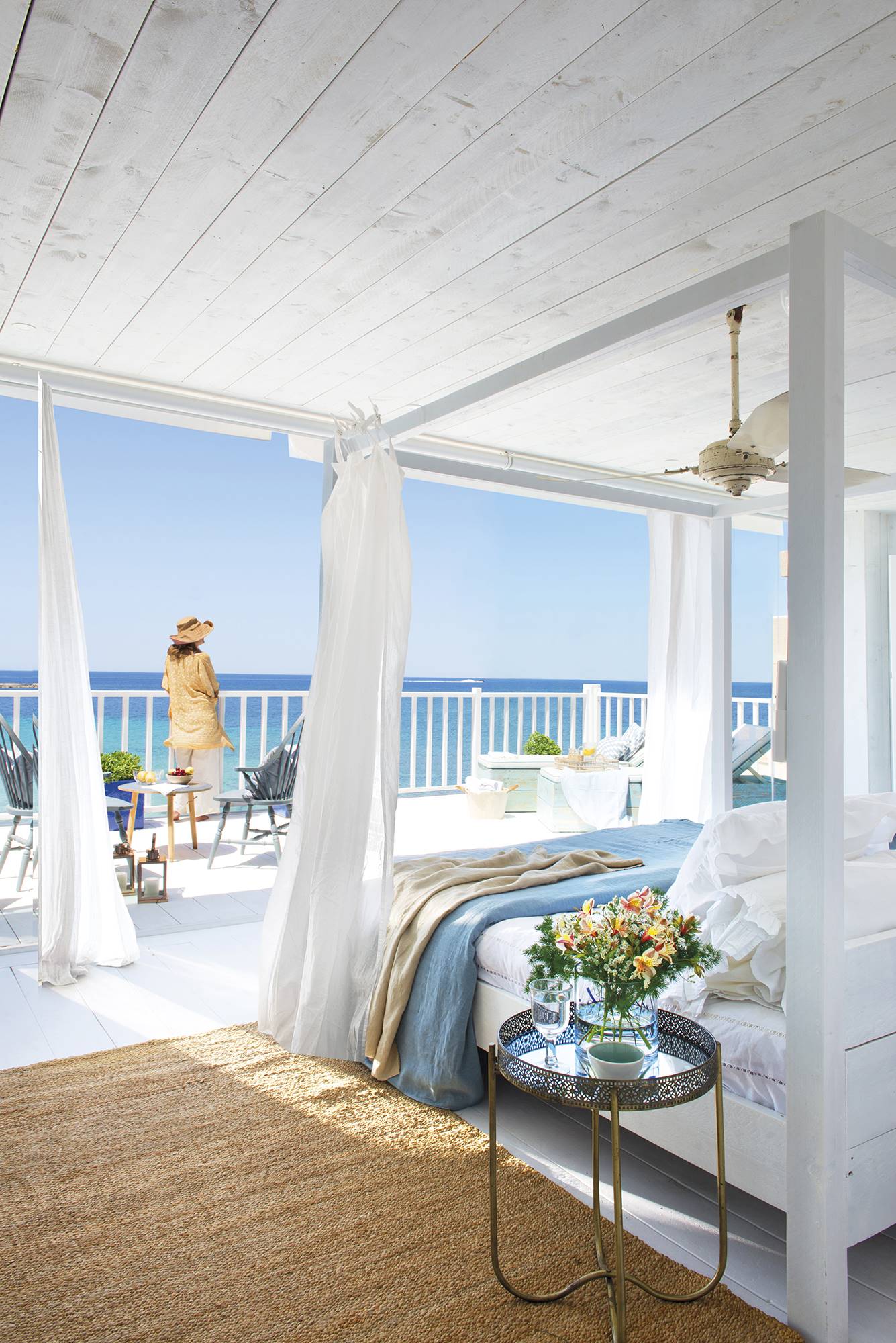 Dormitorio de verano abierto a la terraza decorado en blanco y ropa de cama azul. 