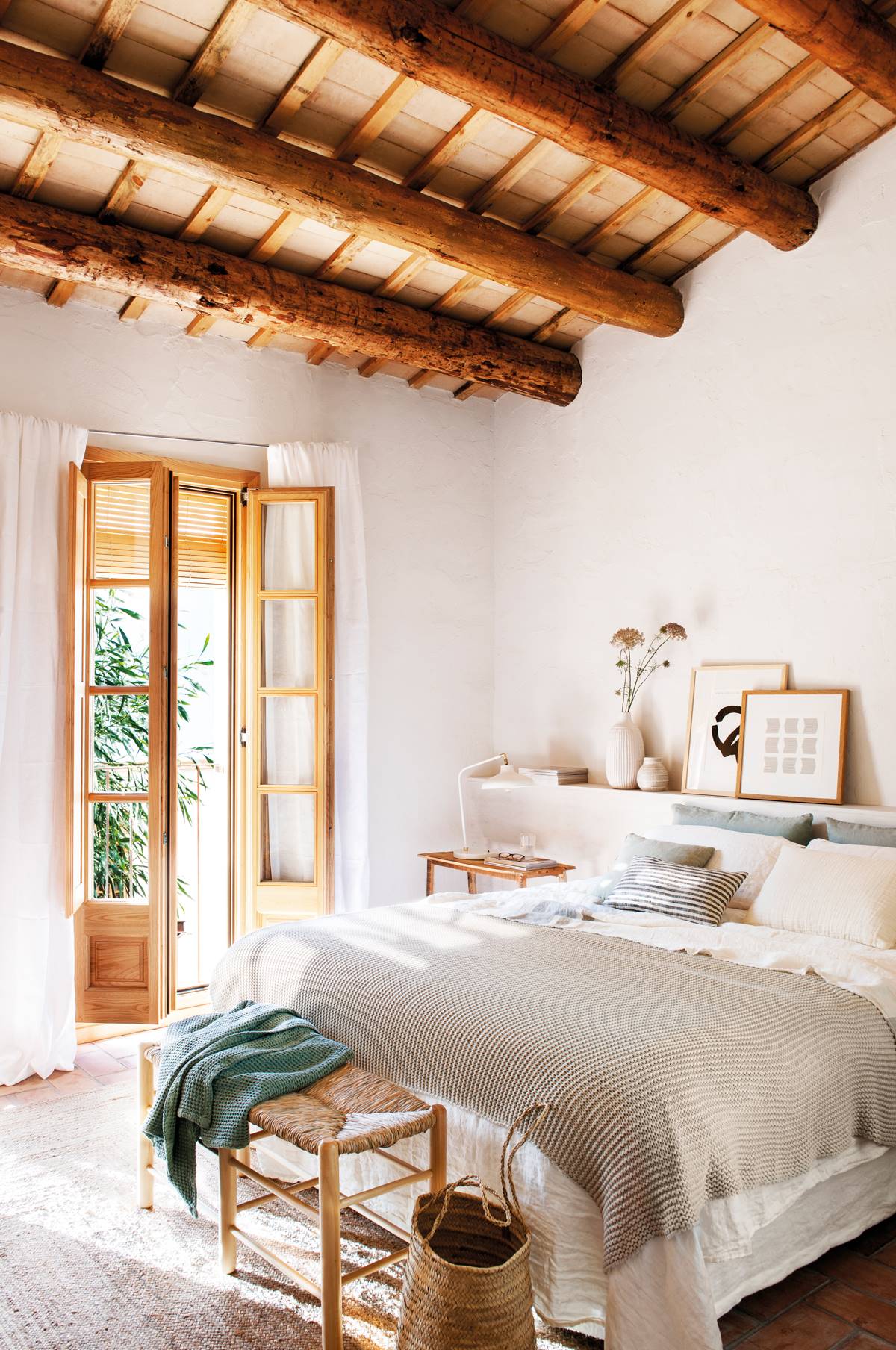 Dormitorio de verano con techo y ventana de madera y textiles de tonos claros. 