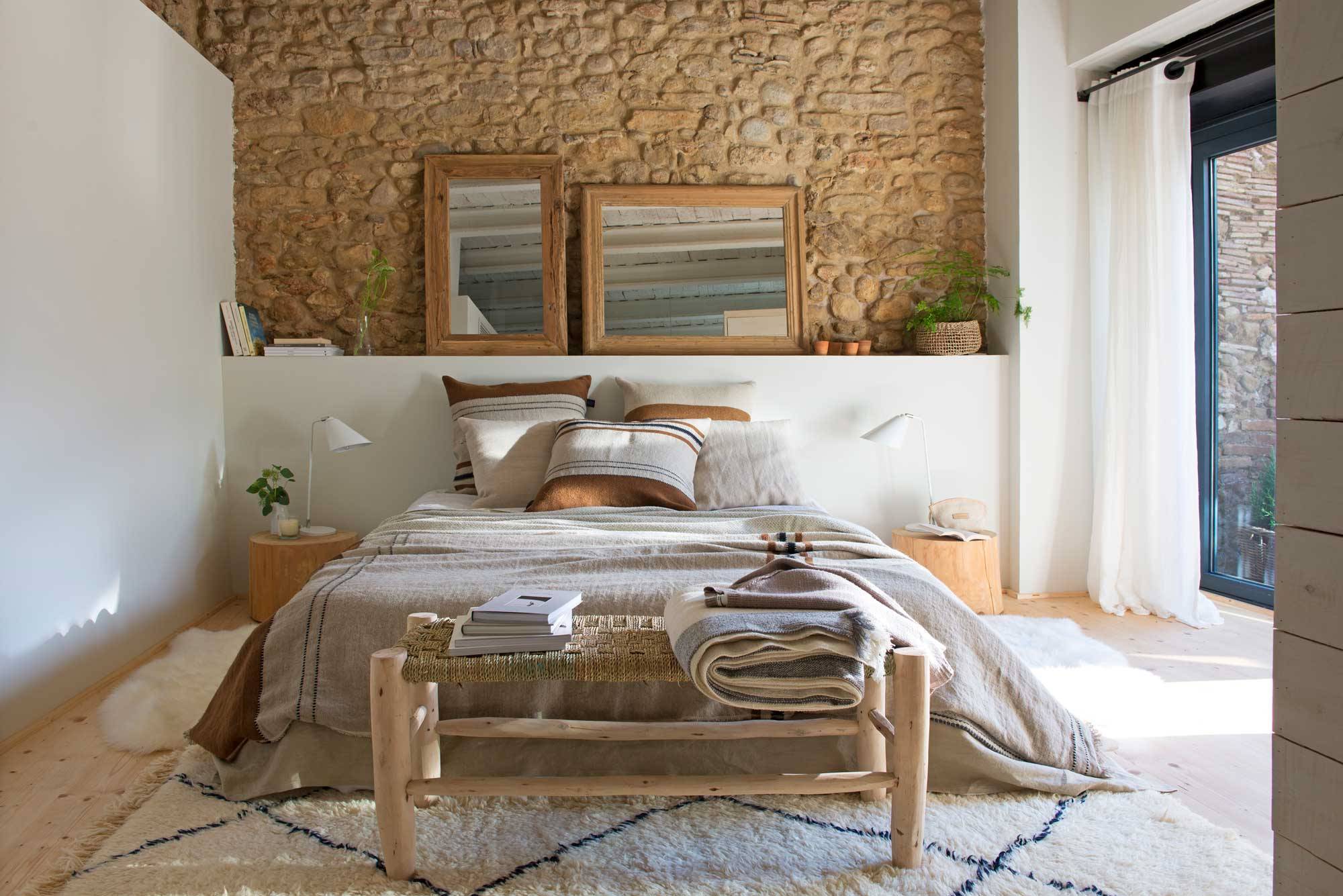 Dormitorio de verano con pared de piedra y ropa de cama de lino beige. 