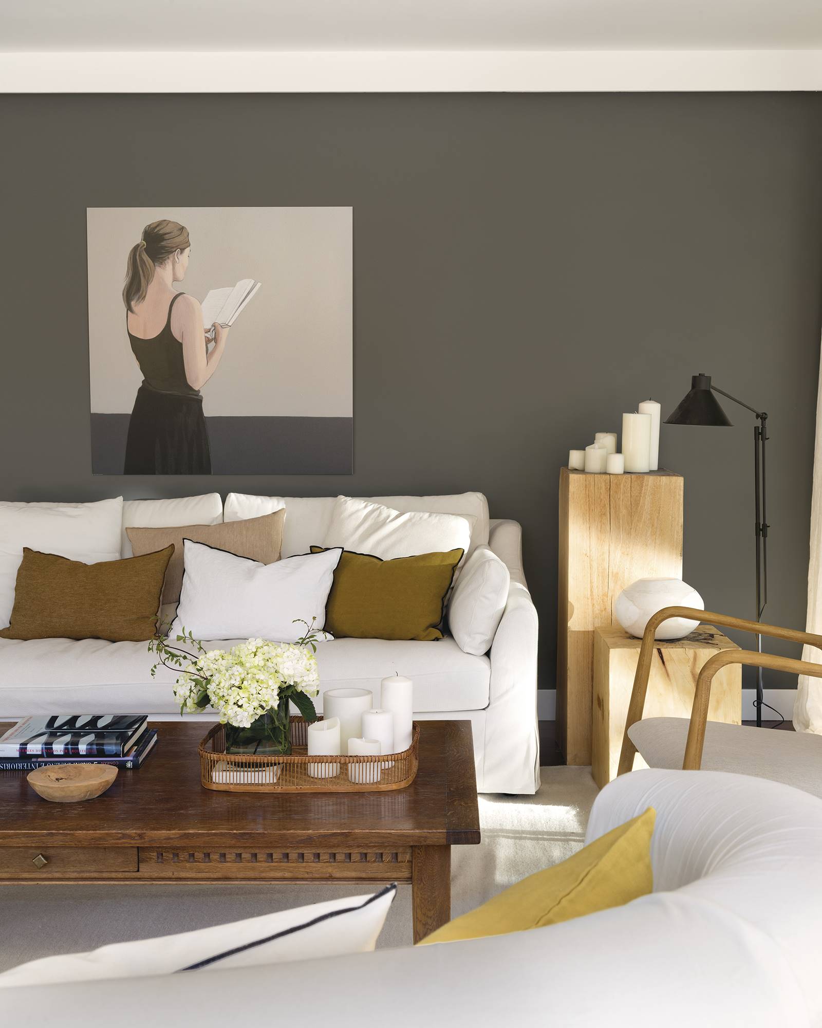 Sofá blanco con textiles en marrón y pared pintada de gris oscuro con cuadro de una mujer de la casa de Paula Duarte.