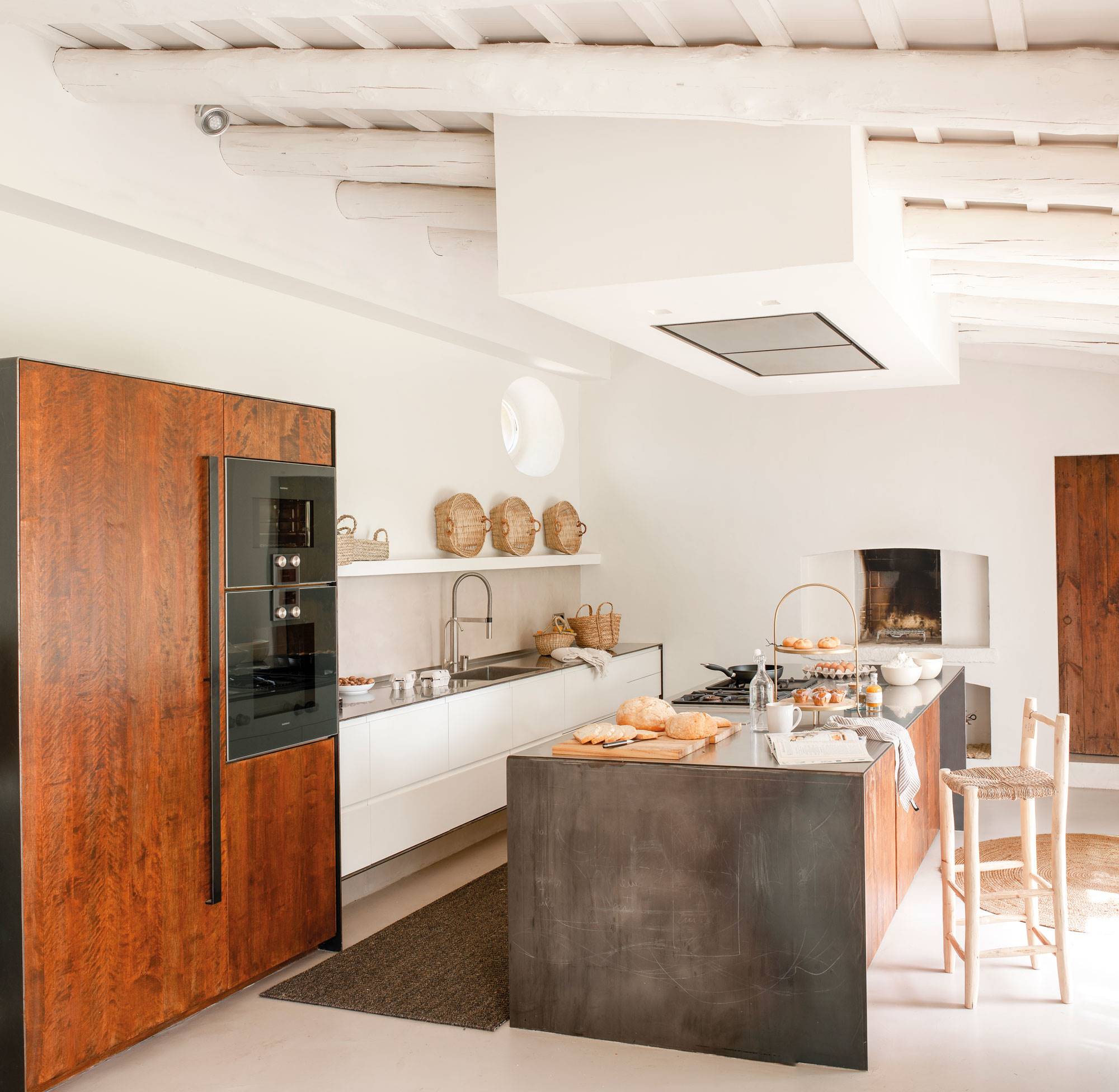 Cocina de estilo rústico moderno con muebles blancos, electrodomésticos panelados en madera y gran isla. 