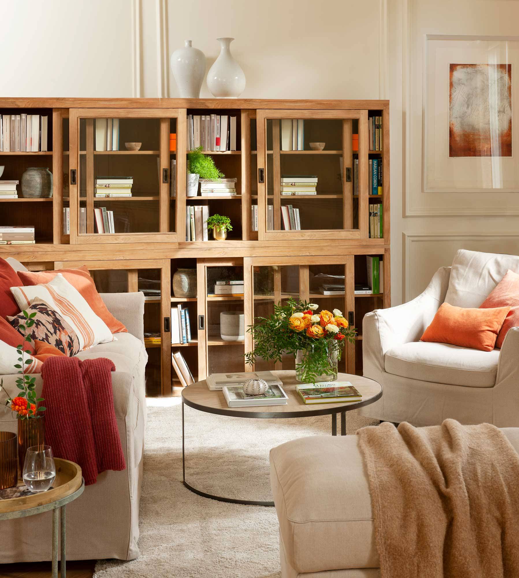 Salón pequeño con librería de madera, sillón blanco y mesa de centro redonda.