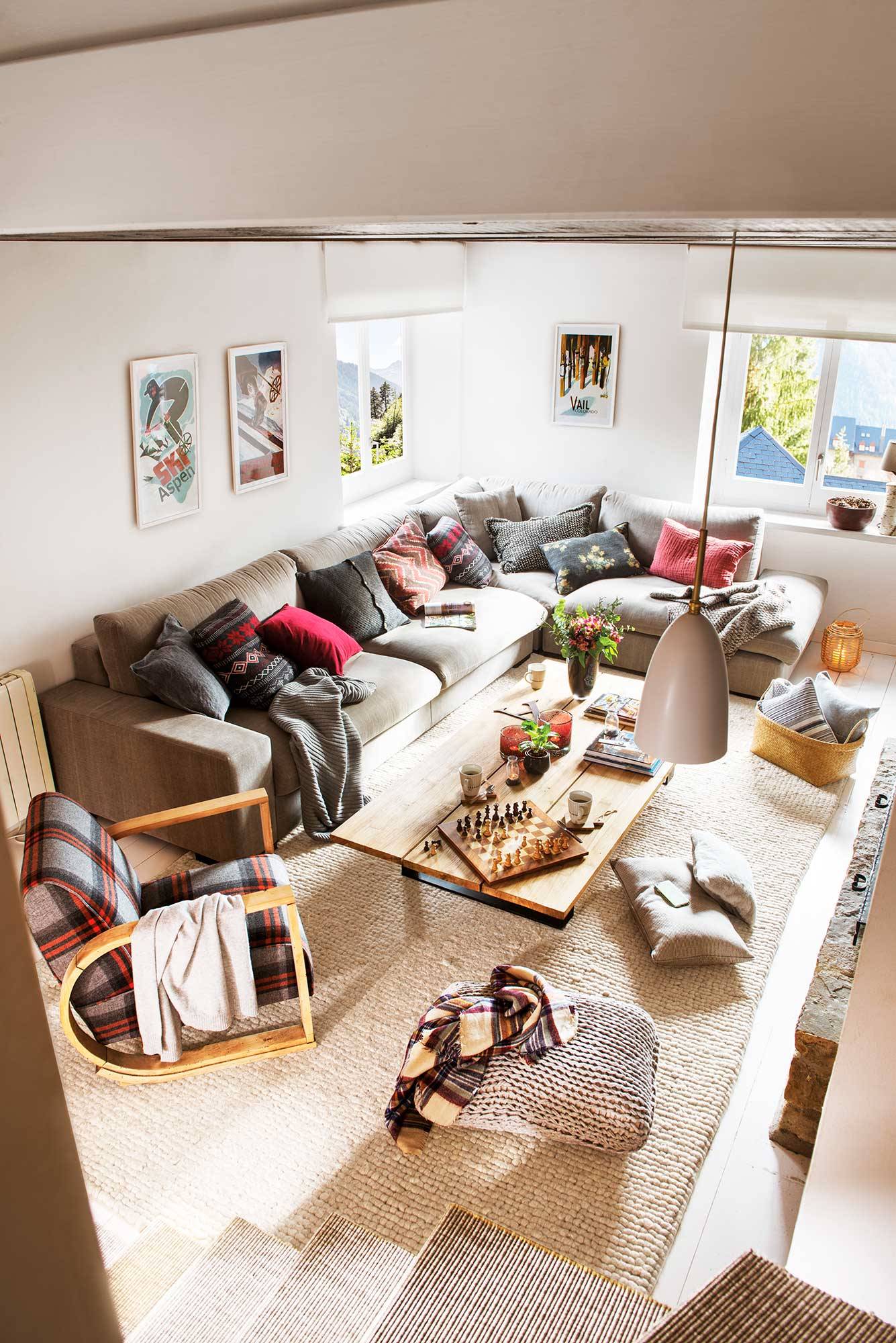 Vista cenital de un salón otoñal de una casa de montaña con el sofá lleno de cojines. 