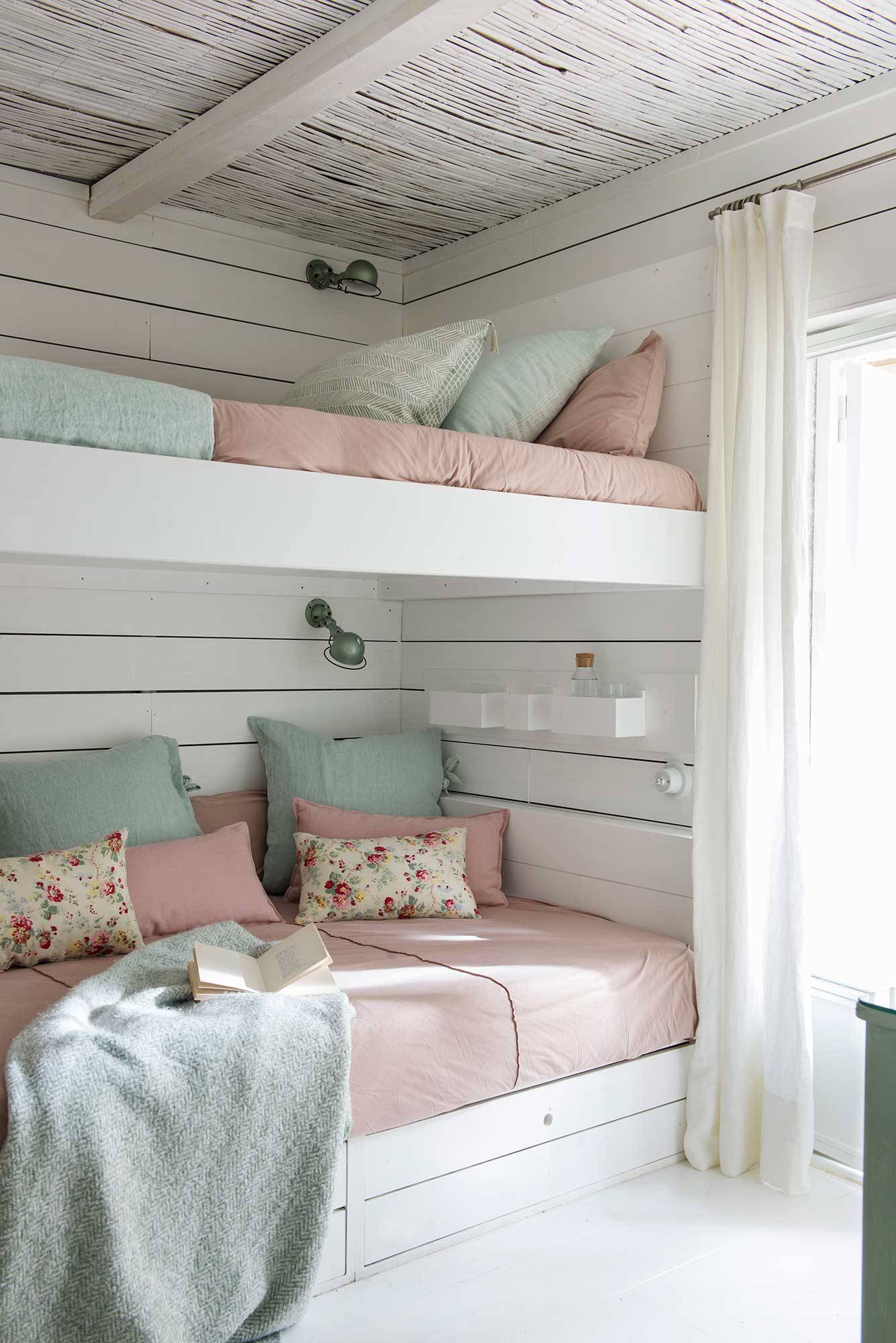 Dormitorio infantil con literas en blanco y ropa de cama rosa.