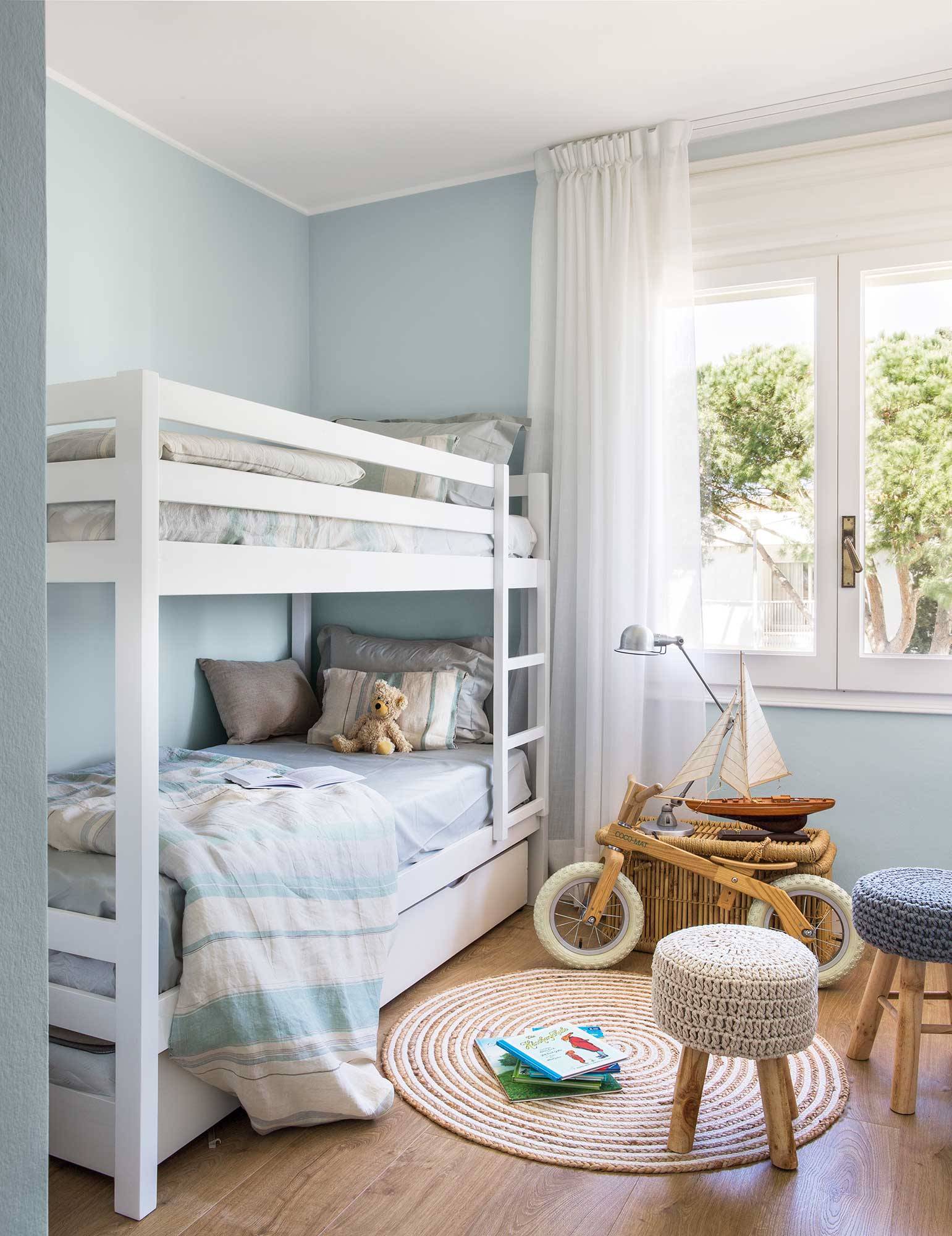 Dormitorio infantil con litera en azul y alfombra y taburetes de fibras.