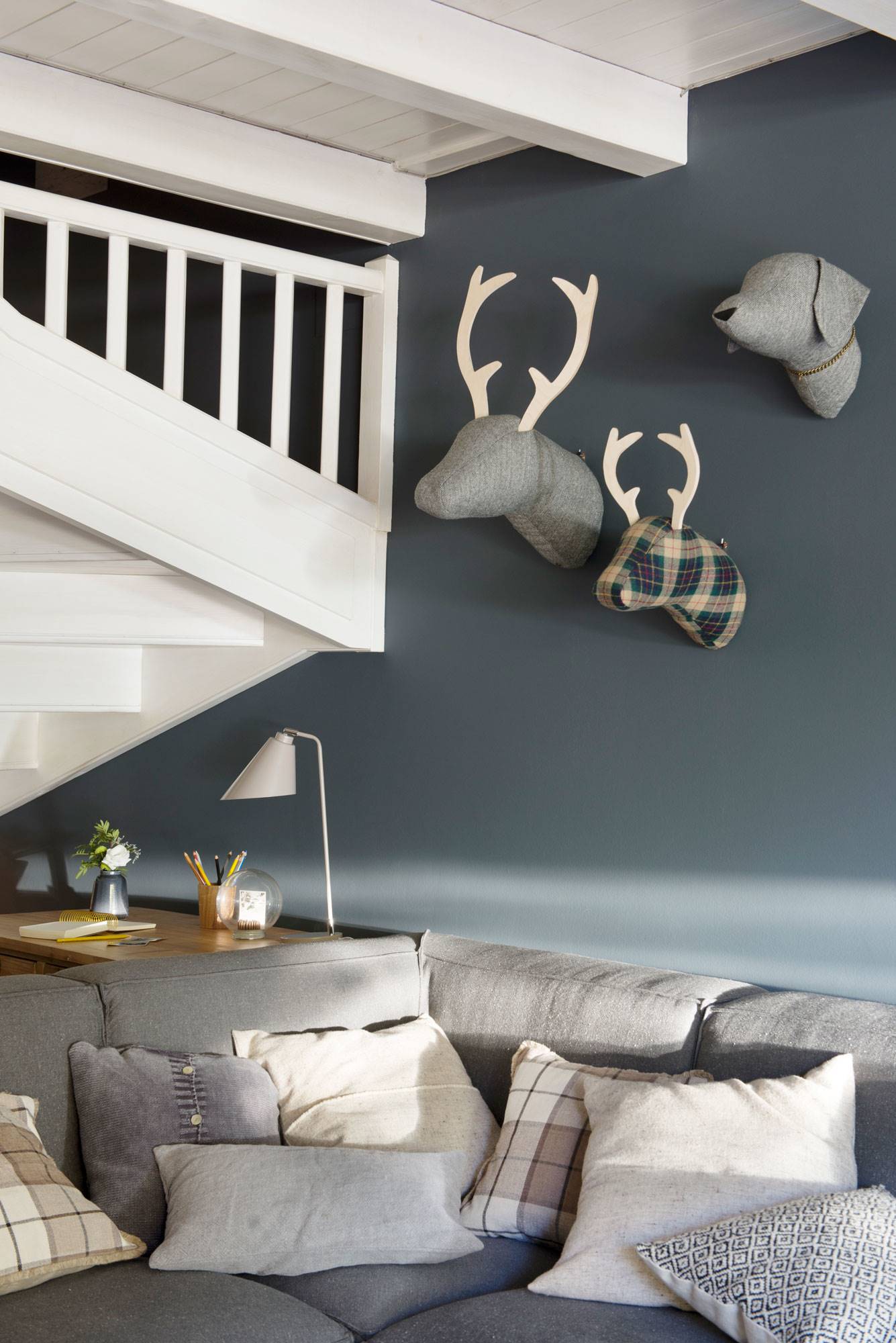 Salón con sofá gris rinconera con cojines de cuadros y lisos y pared azul decorada con animales de tela.