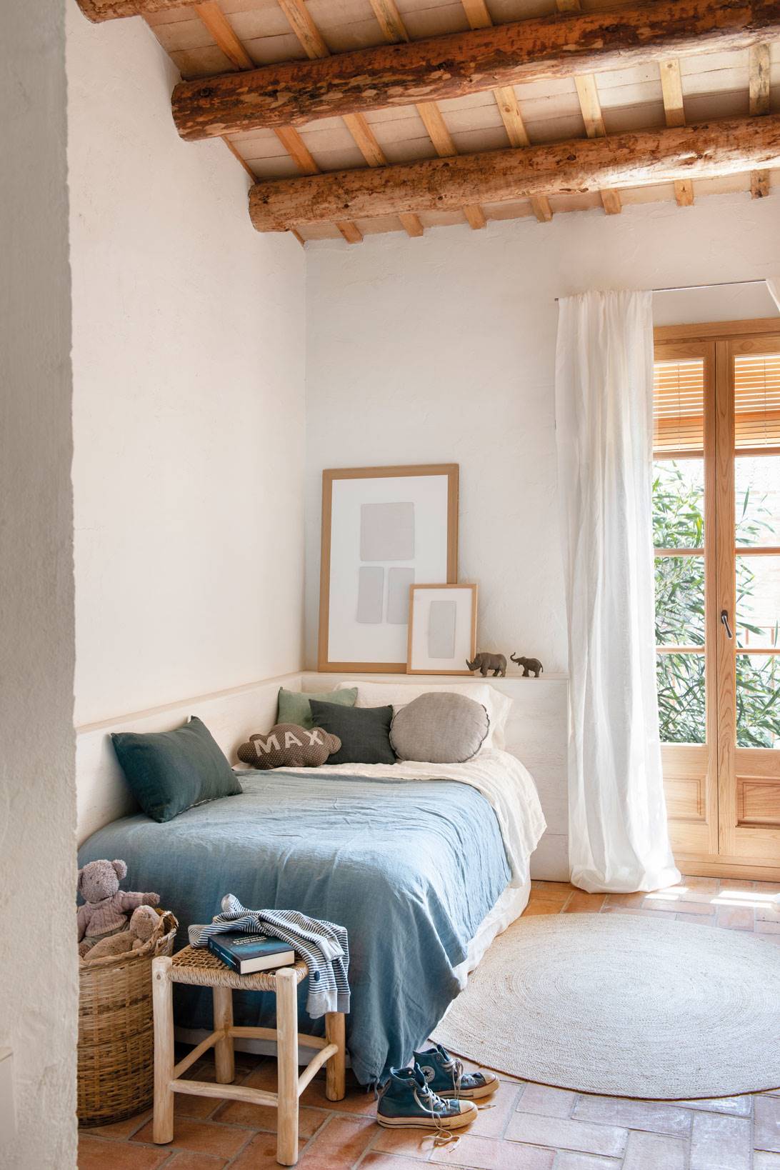 Habitación infantil con vigas de madera, suelo de toba, alfombra y ropa de cama azul.