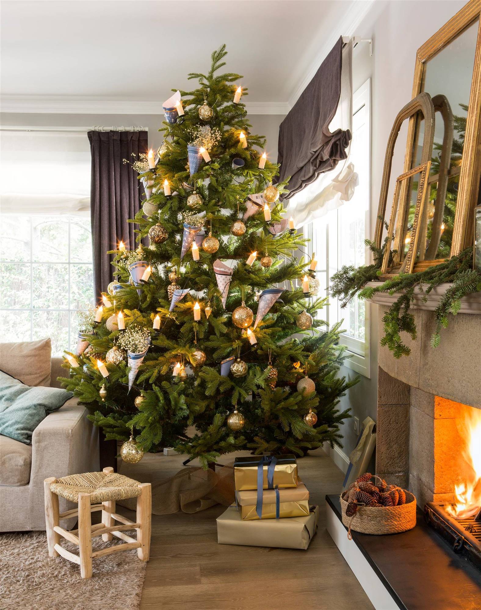 Salón con árbol de Navidad con adornos dorados junto a chimenea. 