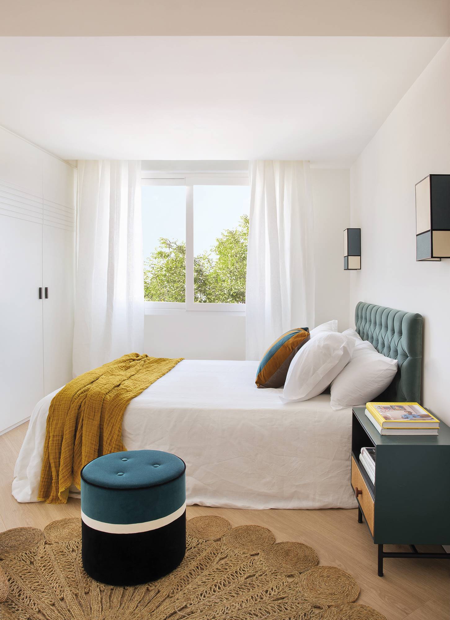 Dormitorio en blanco con toques de azul en cabecero y puff de terciopelo