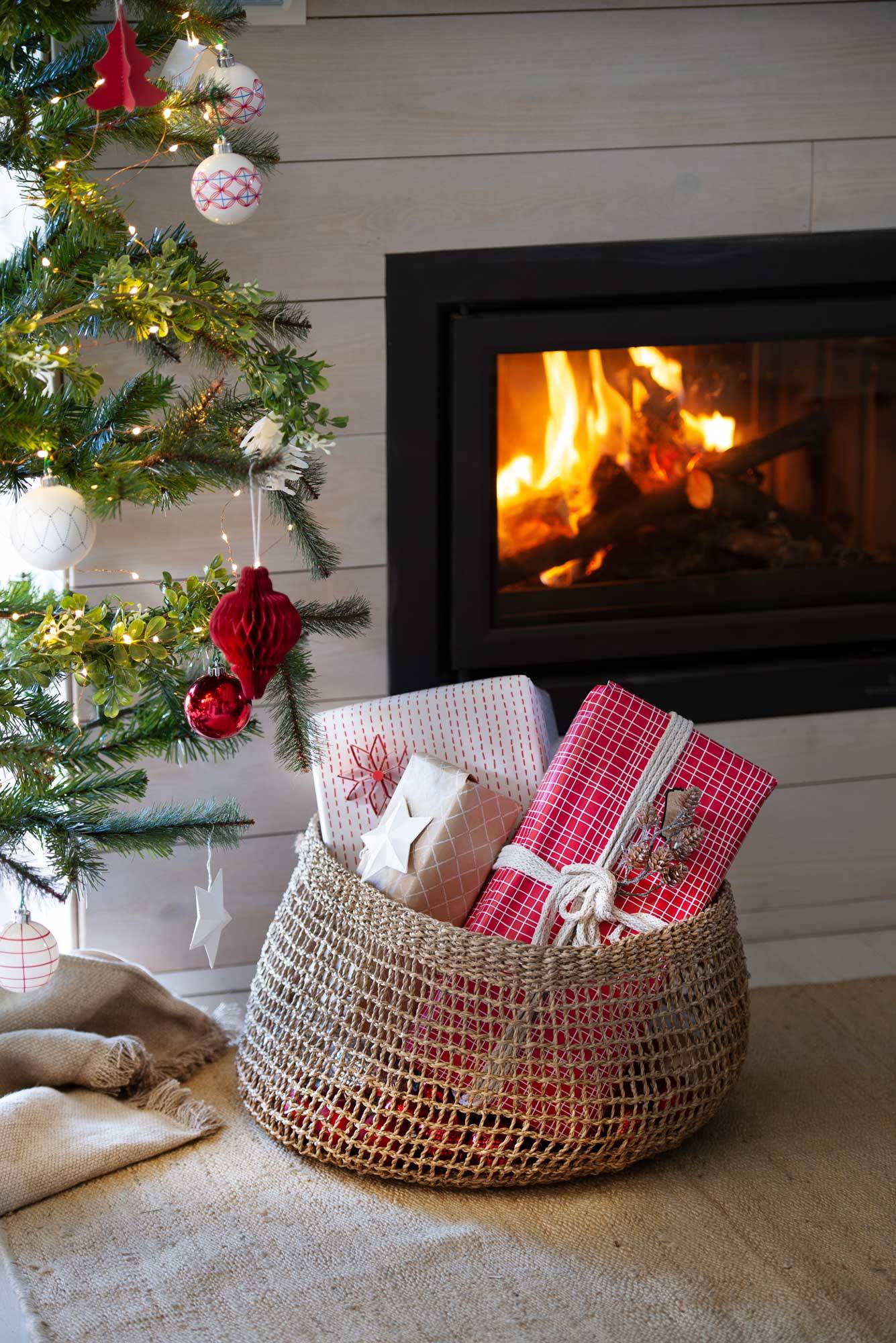 Salón con pie del árbol decorado con cesta en la que hay guardados regalos de Navidad.