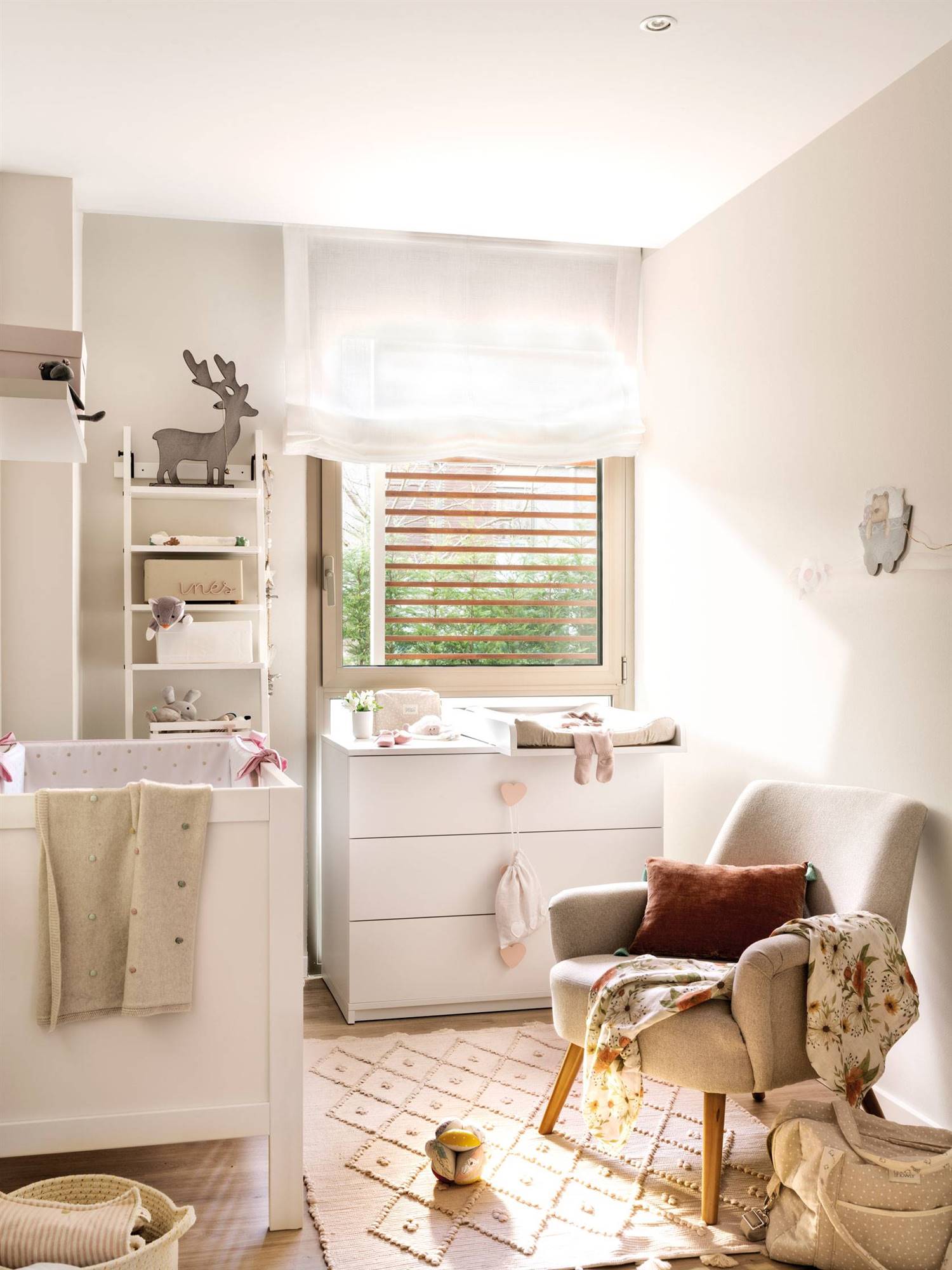 Habitación de bebé en blanco con cuna, cambiador, estantería, butaca y alfombra.