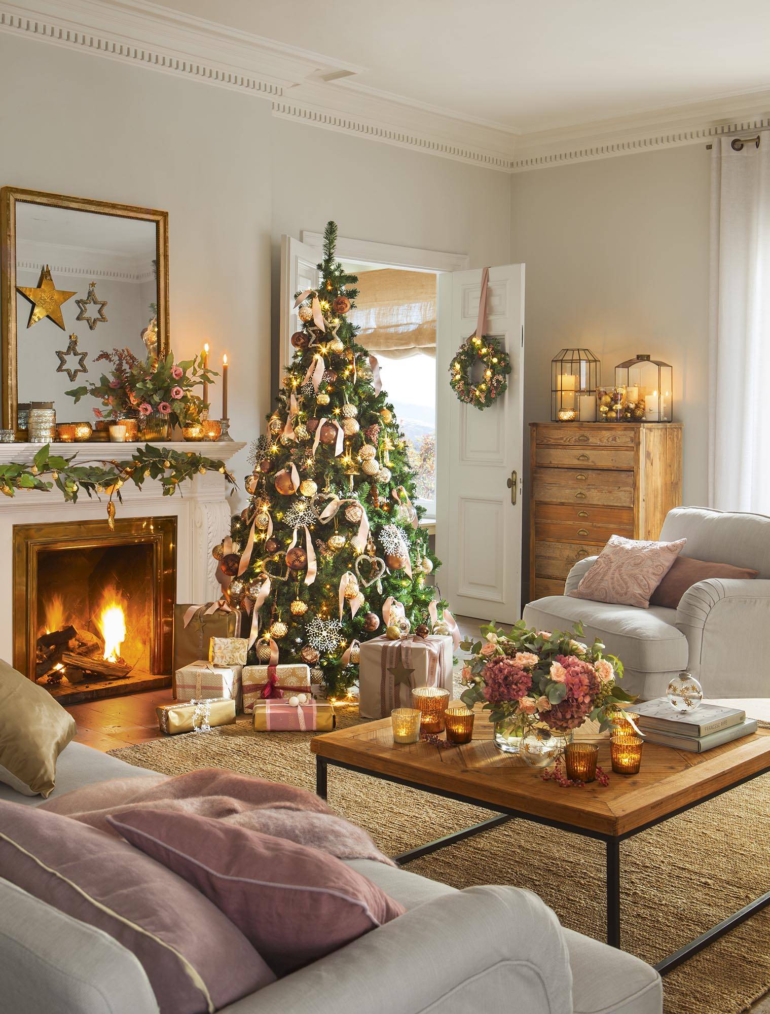Salón con decoración navideña con árbol y detalles dorados y rosas. 