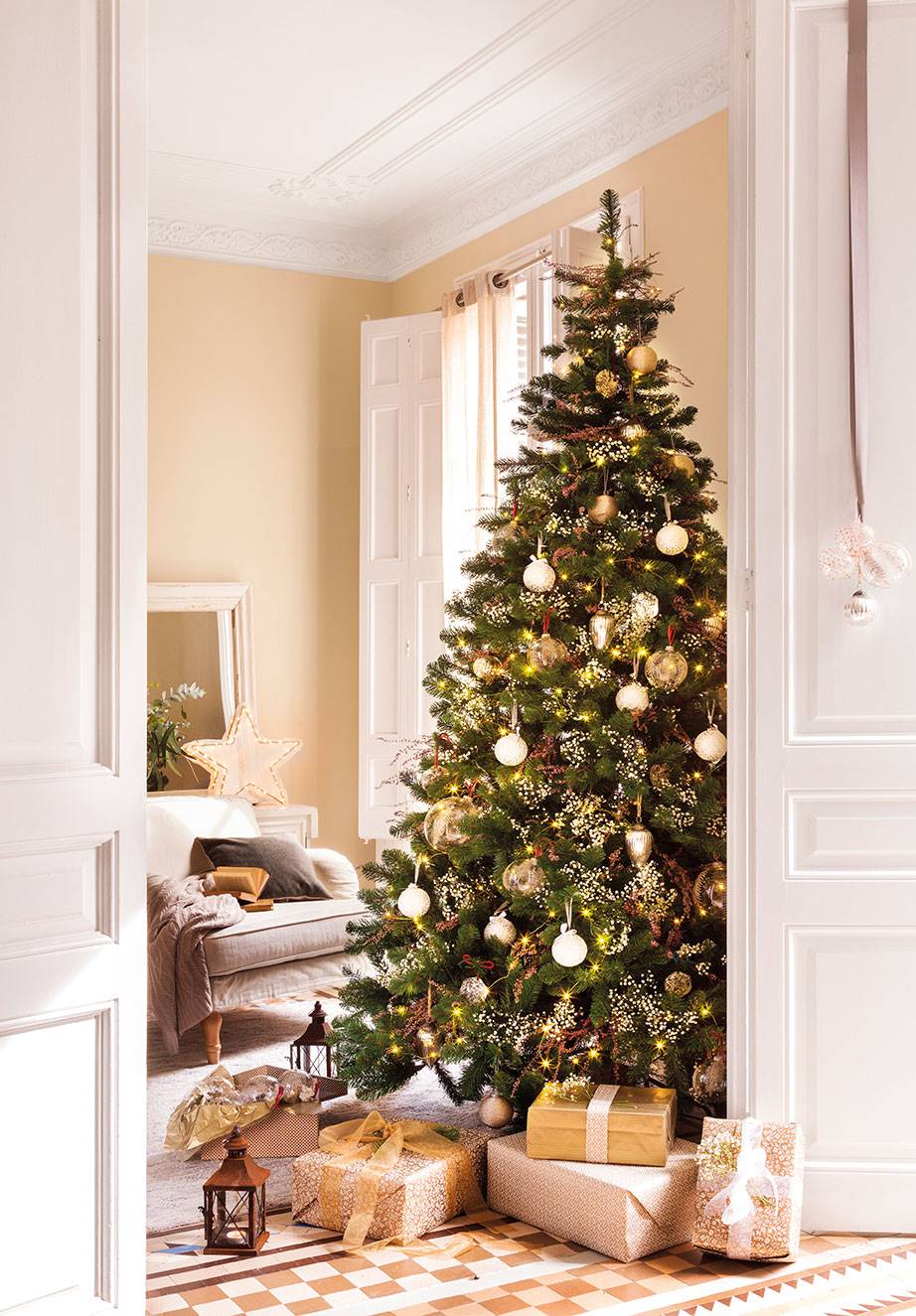 Salón con árbol de Navidad con regalos y puerta blanca con adornos colgados.