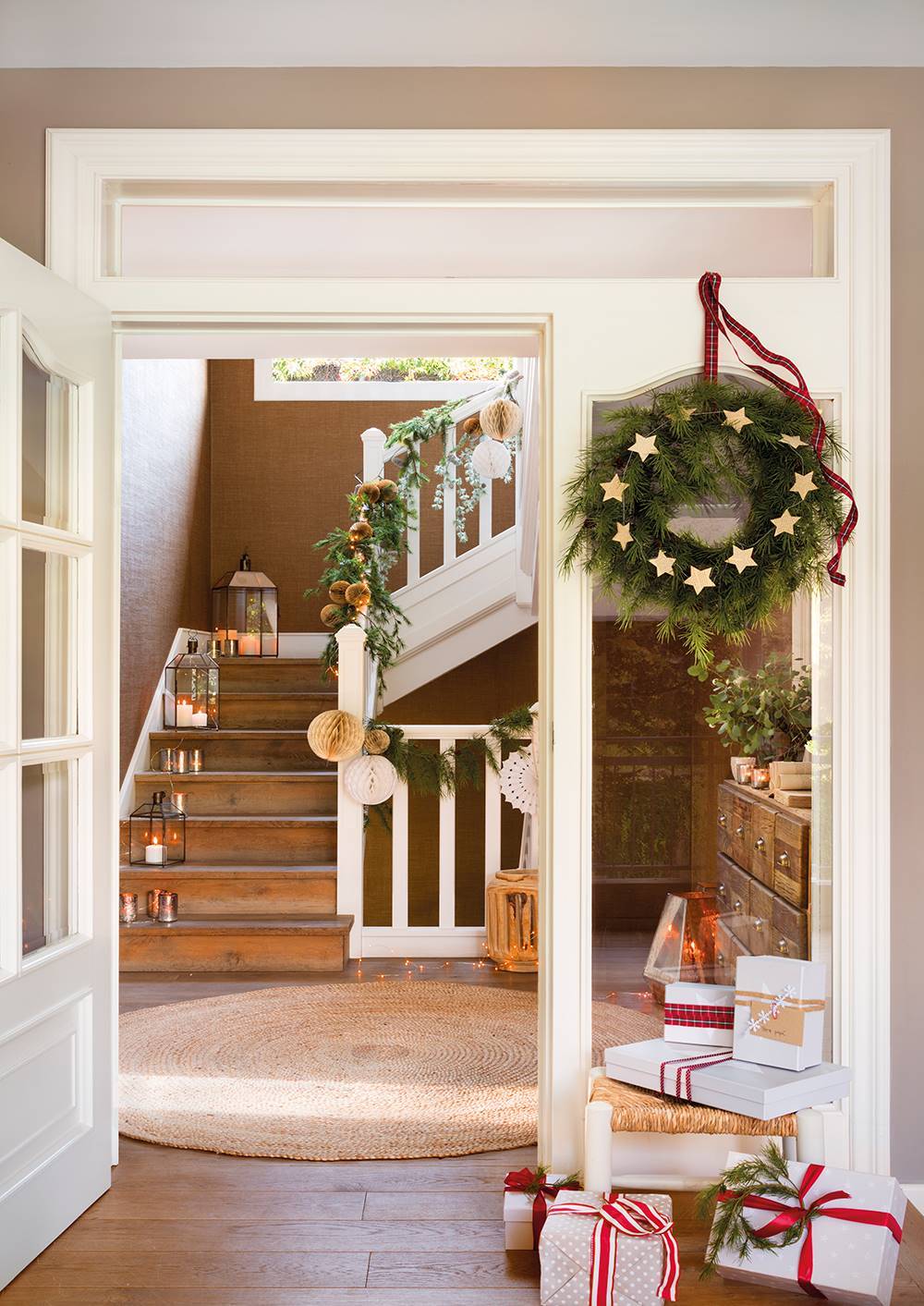 Recibidor con puerta corona de Navidad, regalos y guirnalda en la escalera.