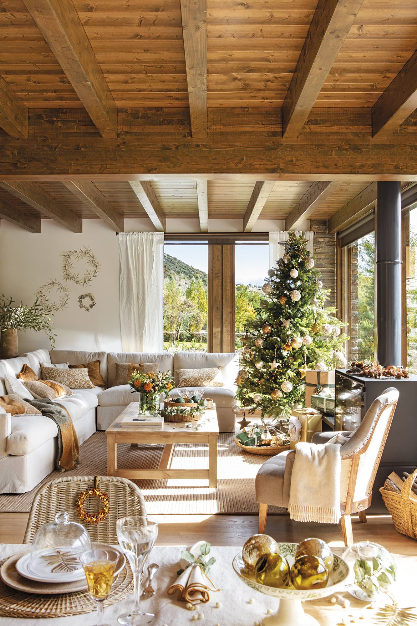 Salón rústico con sofá blanco, árbol de Navidad con adornos dorados y vigas. 