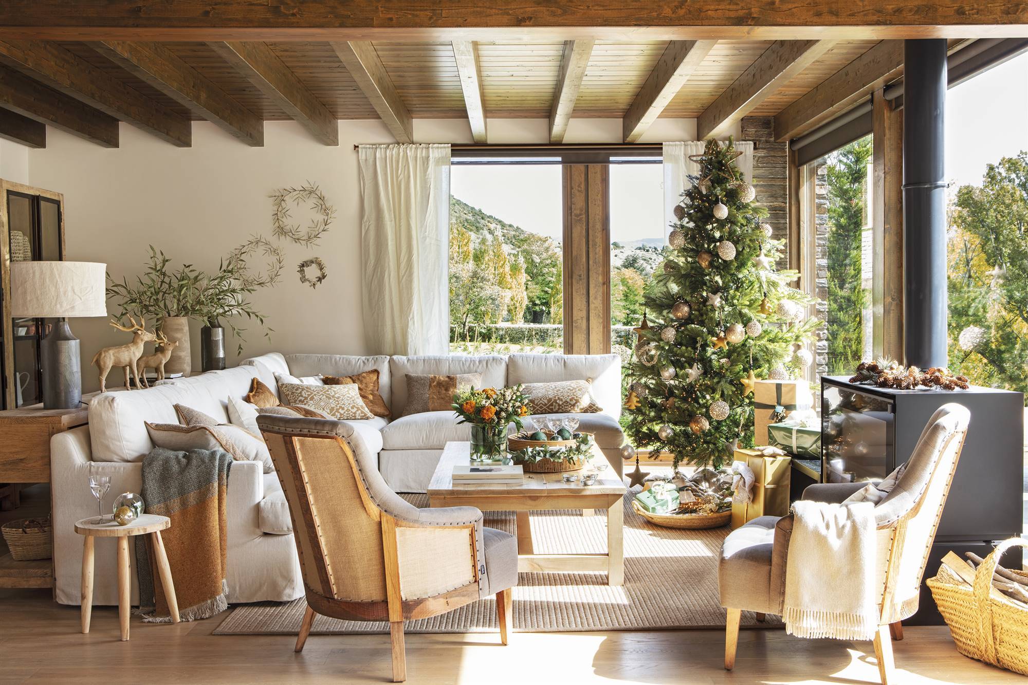 Salón rústico con vigas en el techo, sofá blanco, dos butacas y árbol de Navidad.