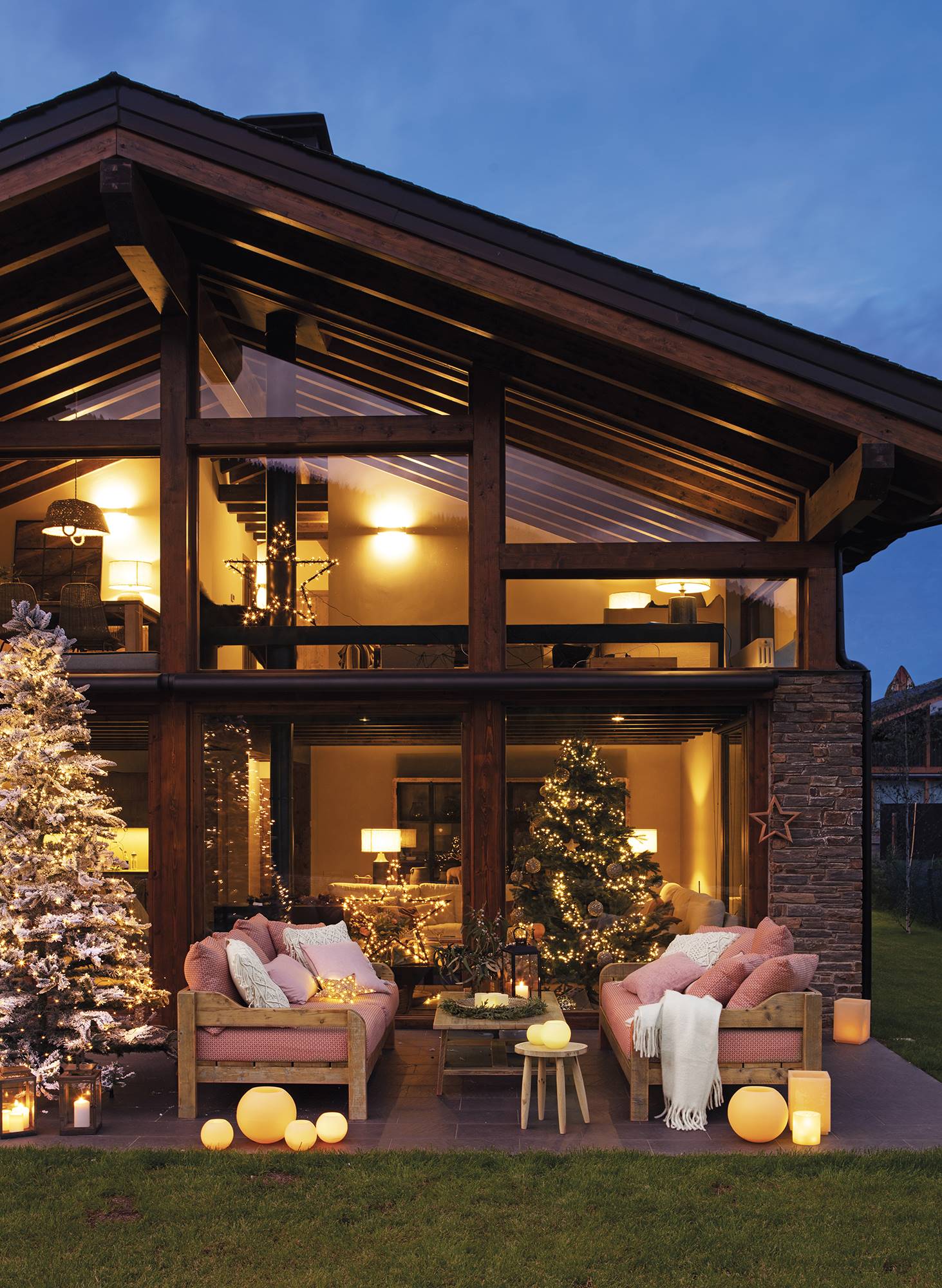 Casa rústica con porche iluminado y decorado de Navidad con guirnaldas, árbol y velas. 