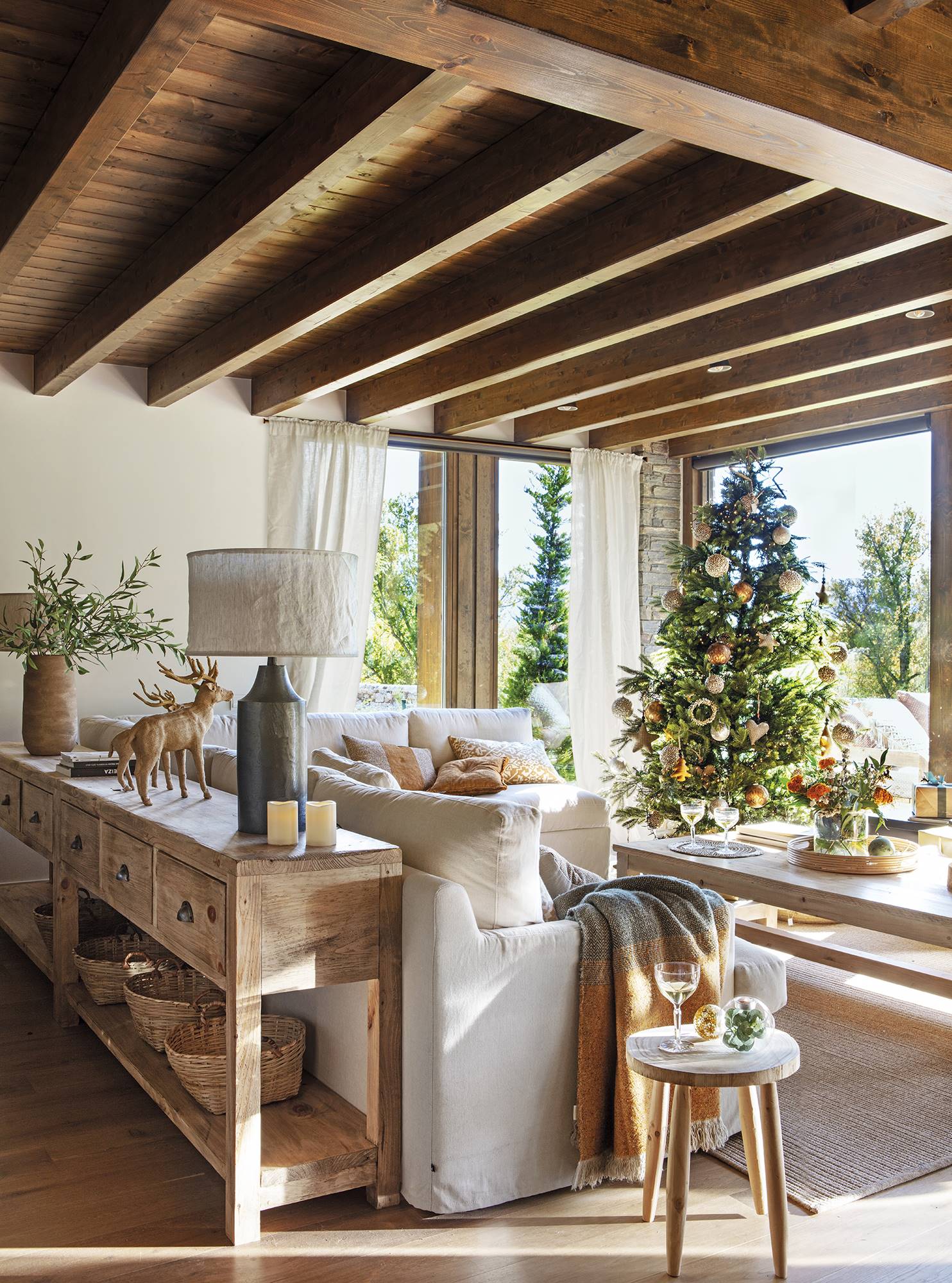 Salón rústico con consola de madera, sofá blanco, vigas y árbol de Navidad.