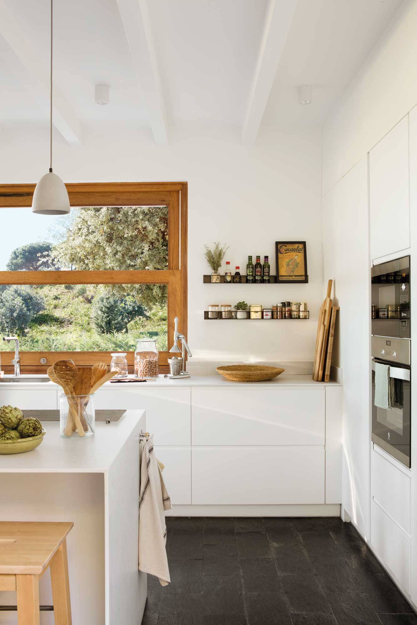 Cocina con muebles blancos, ventana en madera y estantes volados en la pared. 