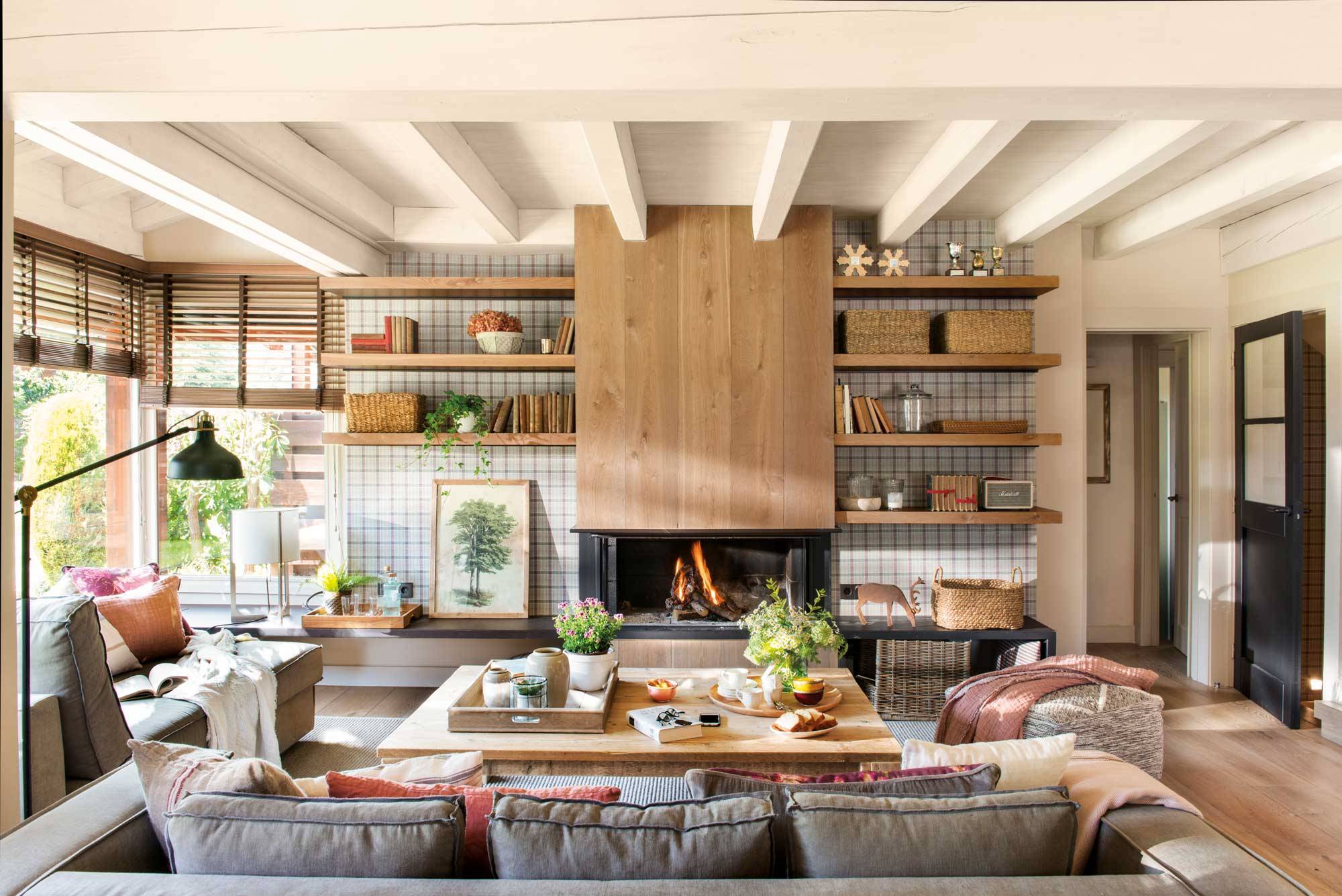 Salón en casa de campo con estilo actual con chimenea, papel pintado a cuadros, estantería y sofás grises.