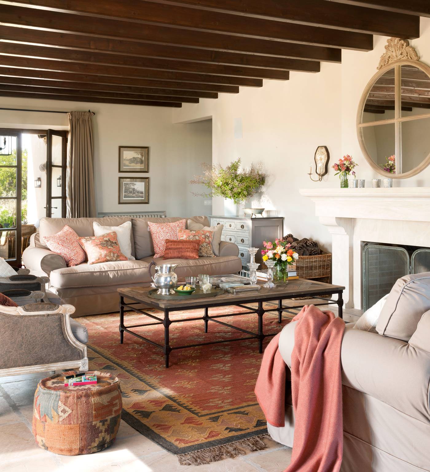 Salón con sofás enfrentados beige, alfombra, cojines, puf y plaid en tonos rosa, terracota, tierra y anaranjado, mesa de centro, chimenea y espejo redondo con moldura superior_368