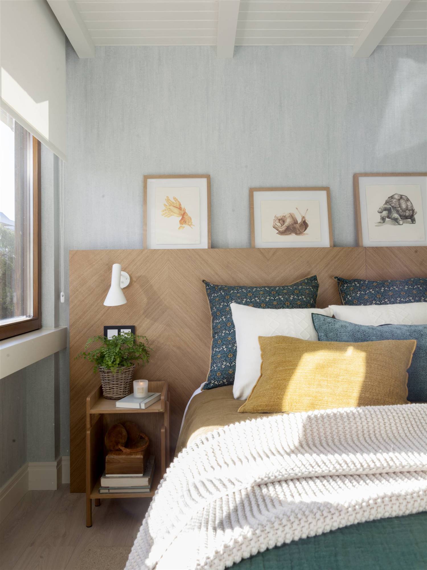 Dormitorio con pared azul y cabecero de madera y tres cuadros apoyados_00522726