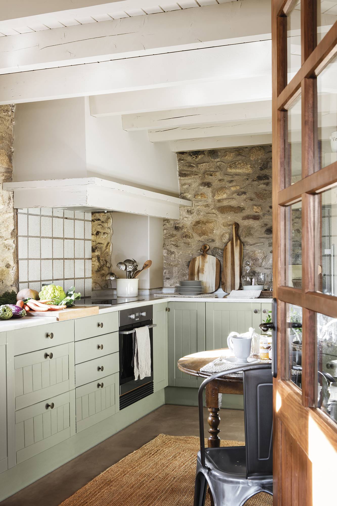 Cocina con muebles bajos de color verde y paredes de piedra. 