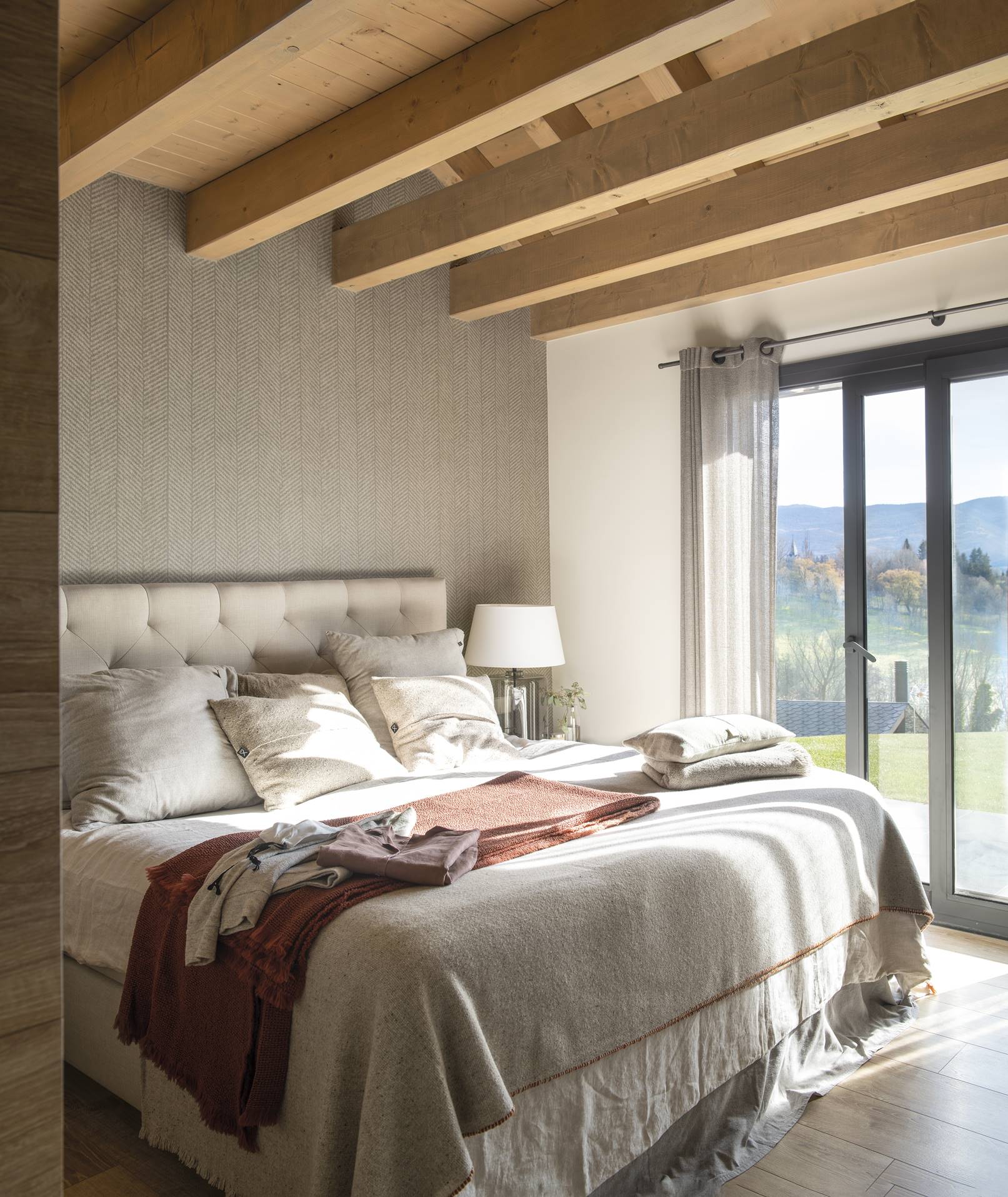 Dormitorio rústico con vigas de madera y cabecero de capitoné tapizado.