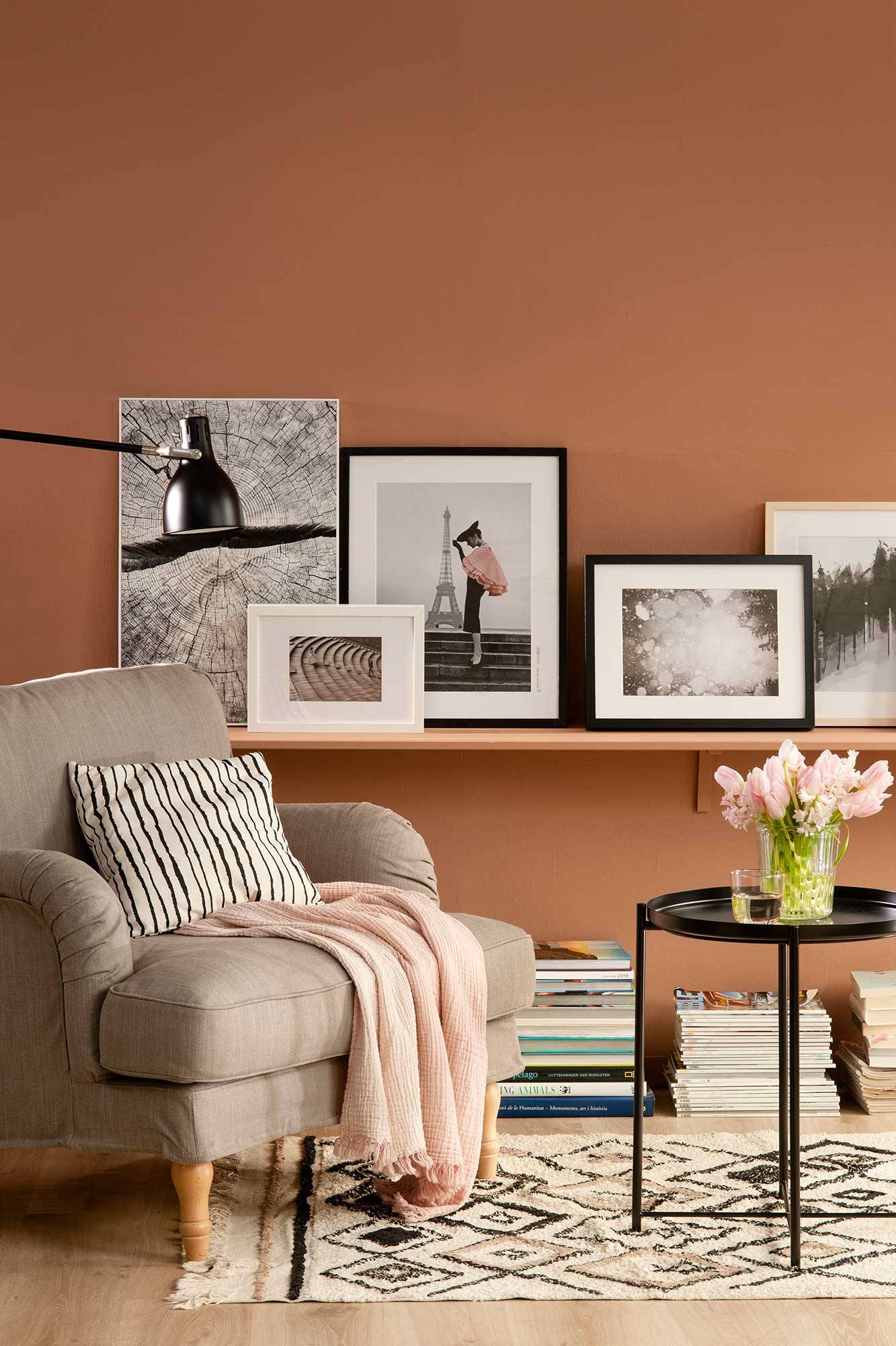Salón con pared marrón con balda y composición de cuadros.