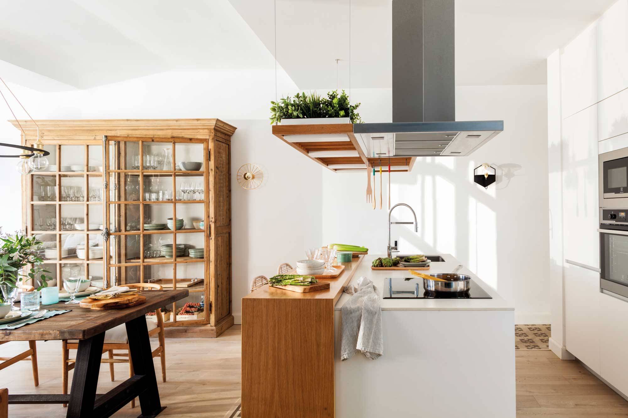 Cocina moderna y abierta con isla con barra de madera y mobiliario blanco. 