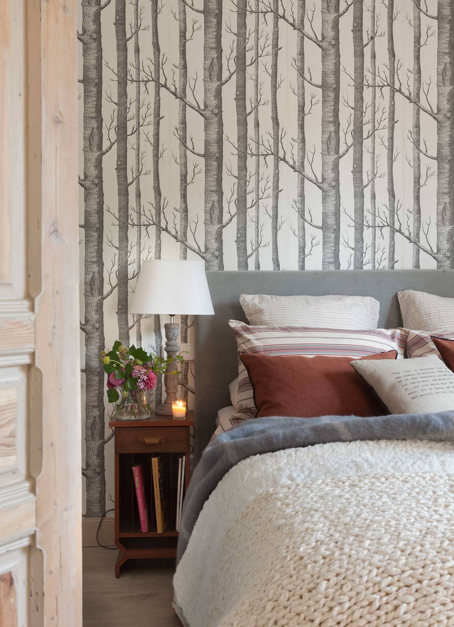 Dormitorio con papel pintado de árboles en la pared del cabecero.
