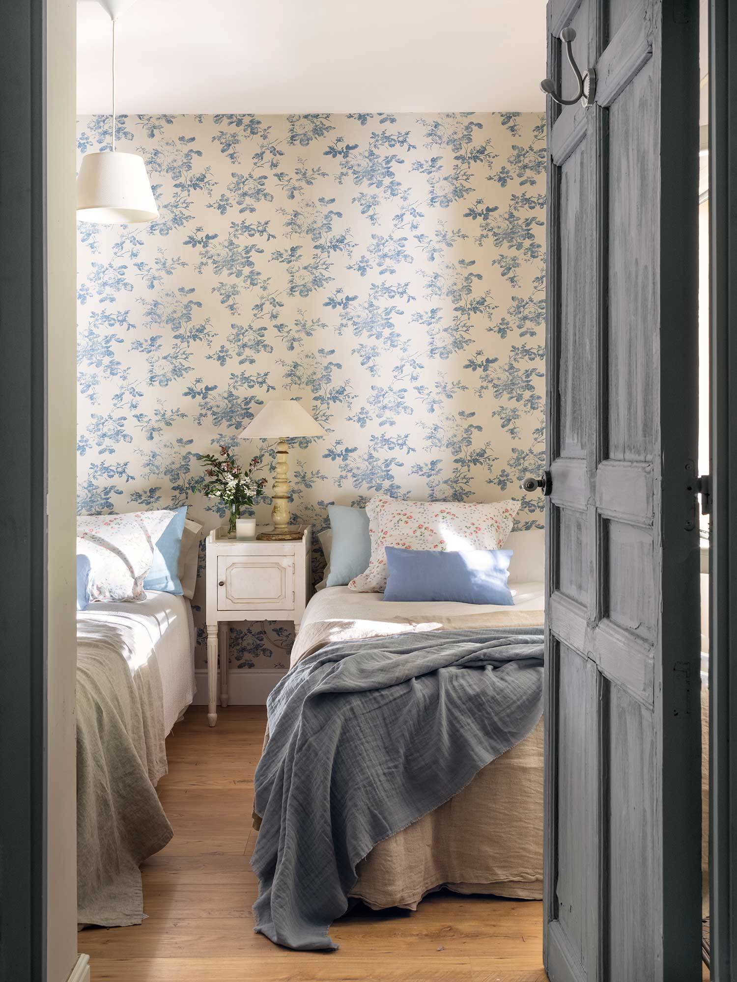Habitación infnatil con muebles blancos y papel pintado de flores azules.