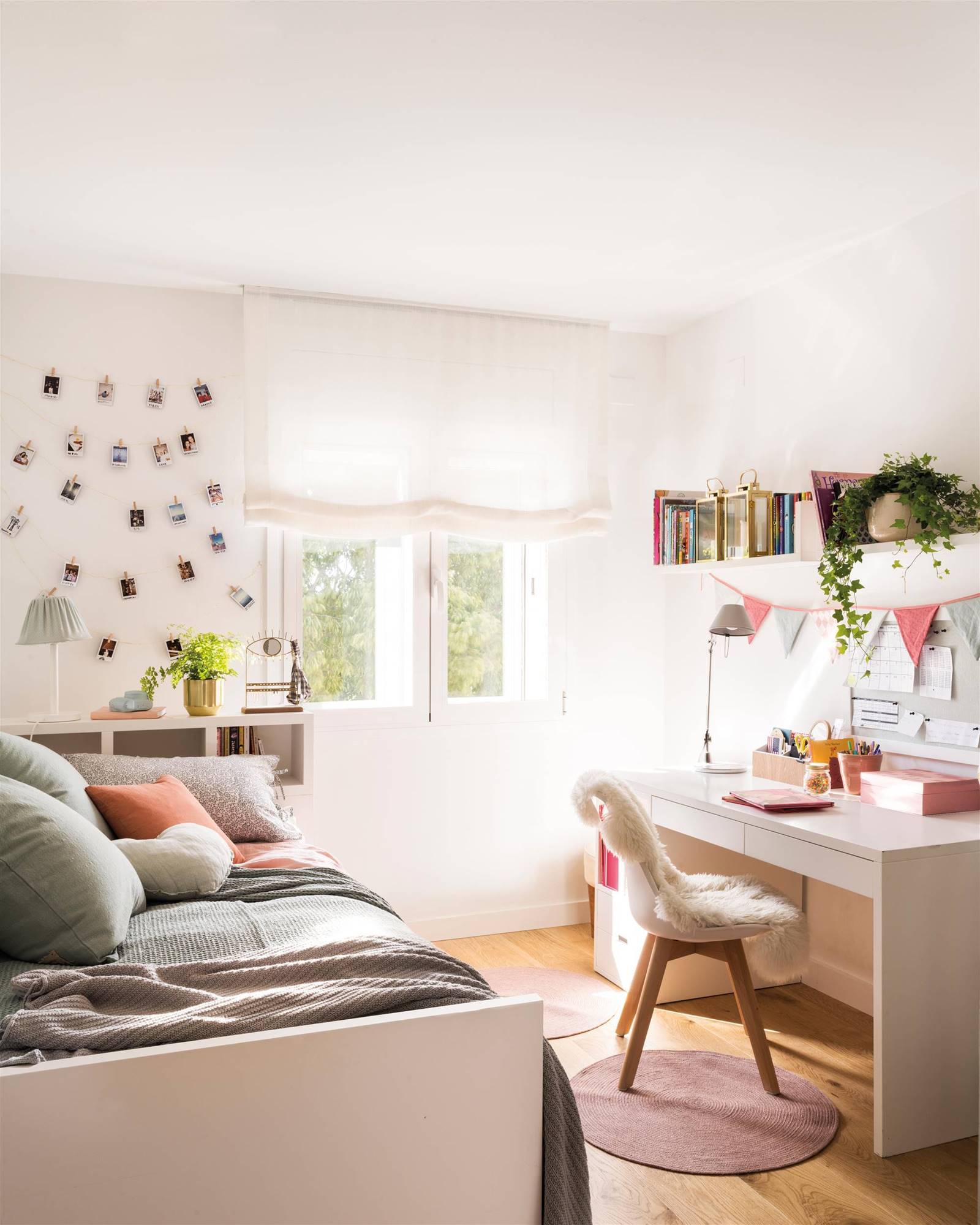 Dormitorio infantil con escritorio blanco, silla, cama, estor en la ventana y fotos colgadas en la pared. 