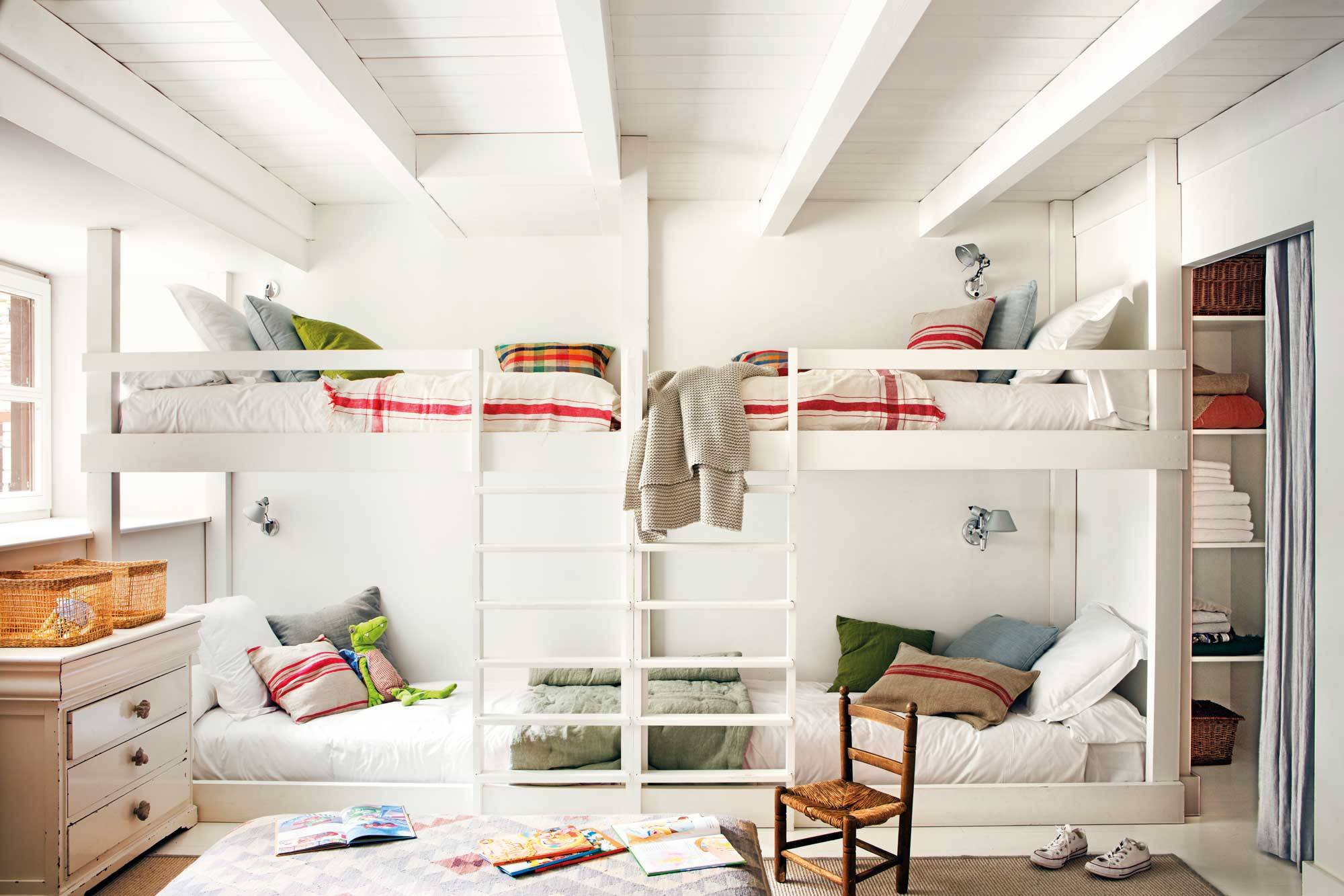 Habitación infantil con varias camas litera en blanco y cojines de colores. 